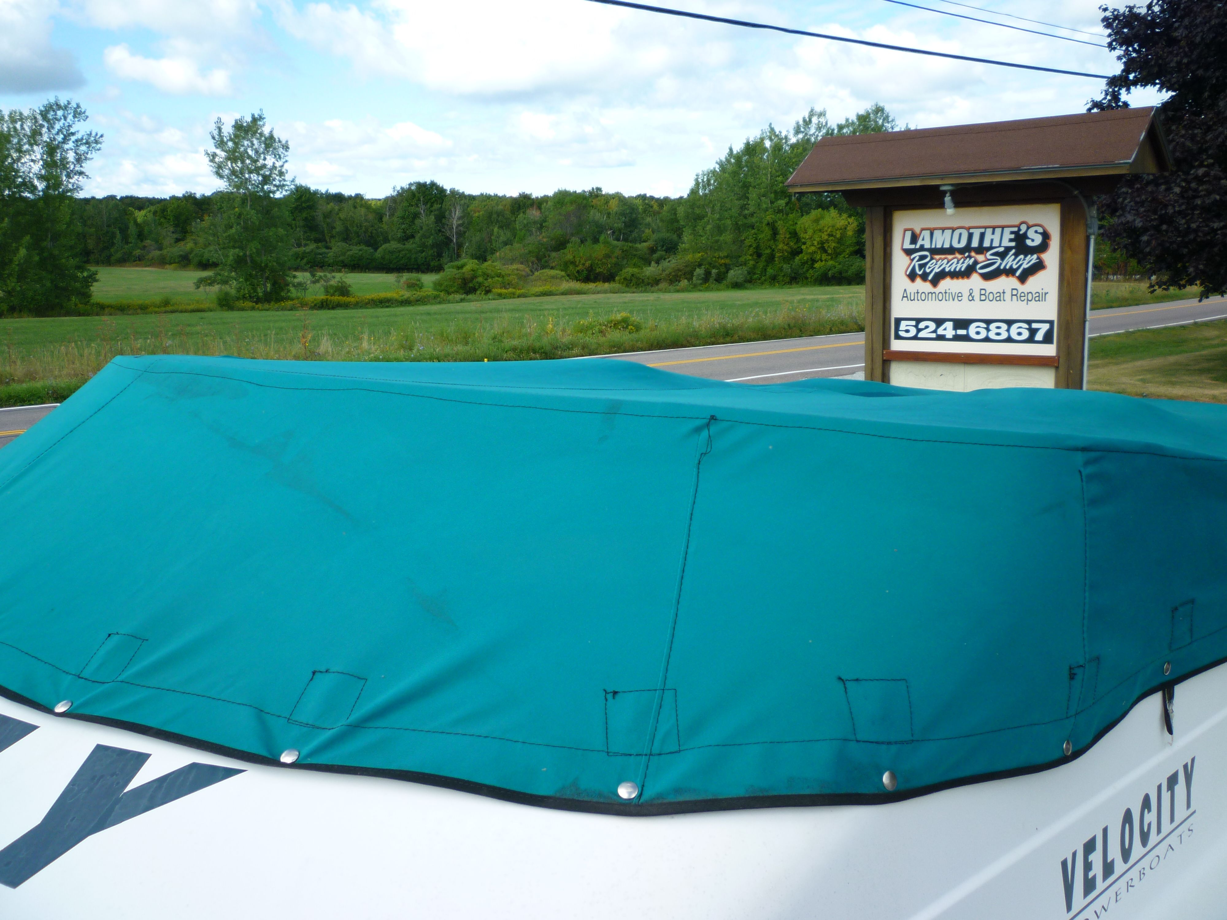 Covered Velocity 280 boat near Lamothe's Repair Shop sign, surrounded by greenery.