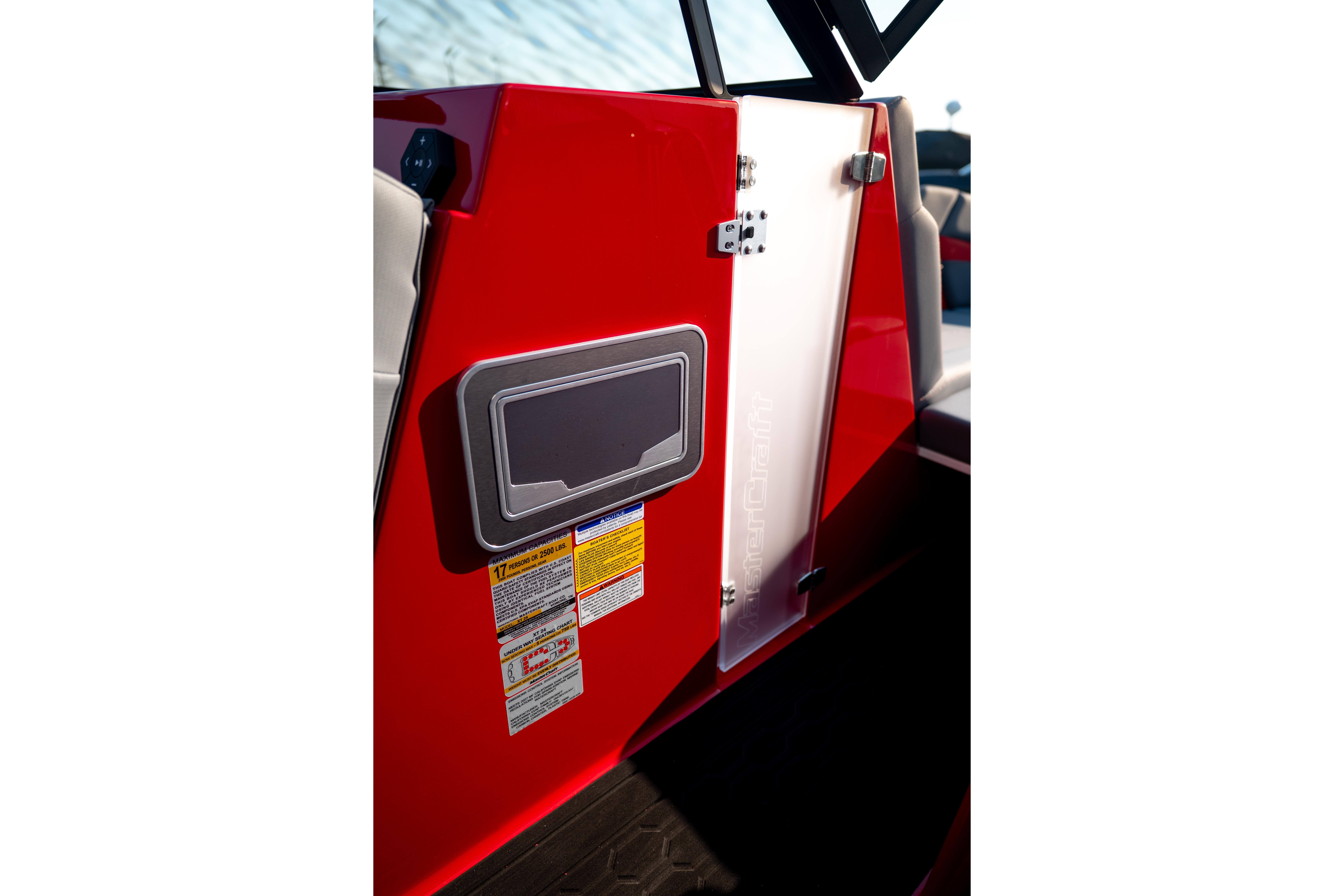 Red 2027 MasterCraft XT24 boat interior with safety labels and storage compartment.