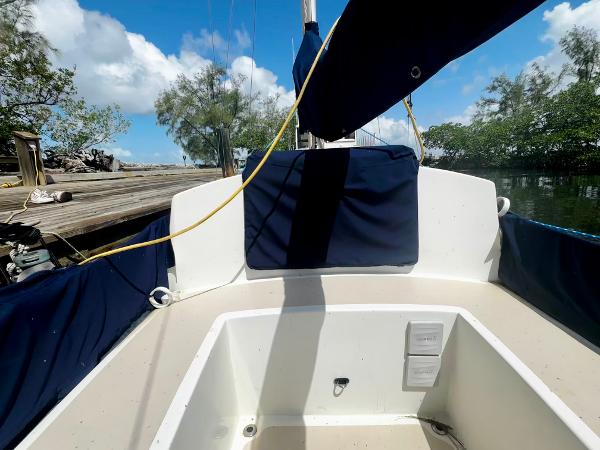 1968 Sailboat 24 cockpit with blue covers, docked near lush greenery and clear sky.