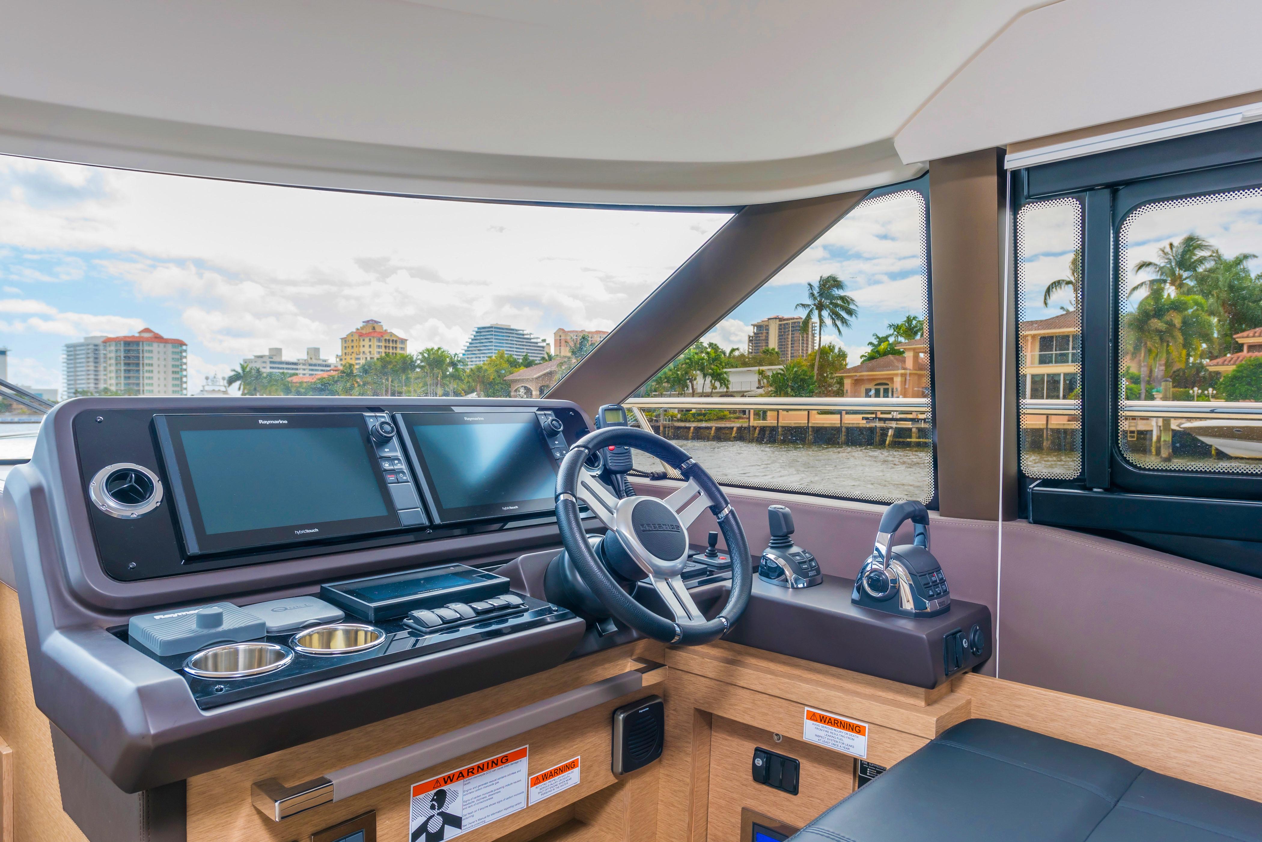 Prestige 460 Flybridge 2025 yacht helm station with modern navigation systems and waterfront view.