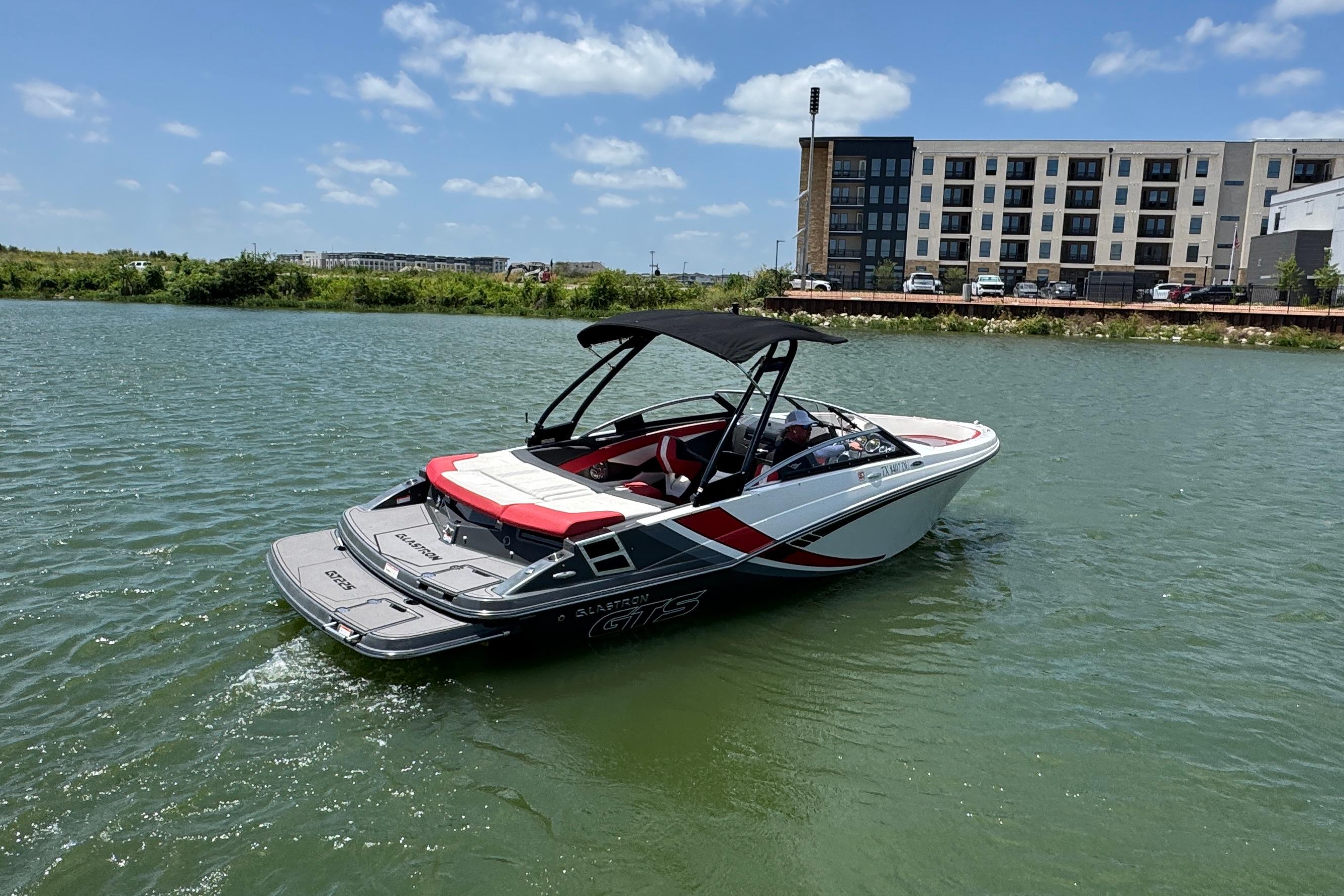 2017 Glastron GT 225 boat cruising on a sunny day near modern buildings.