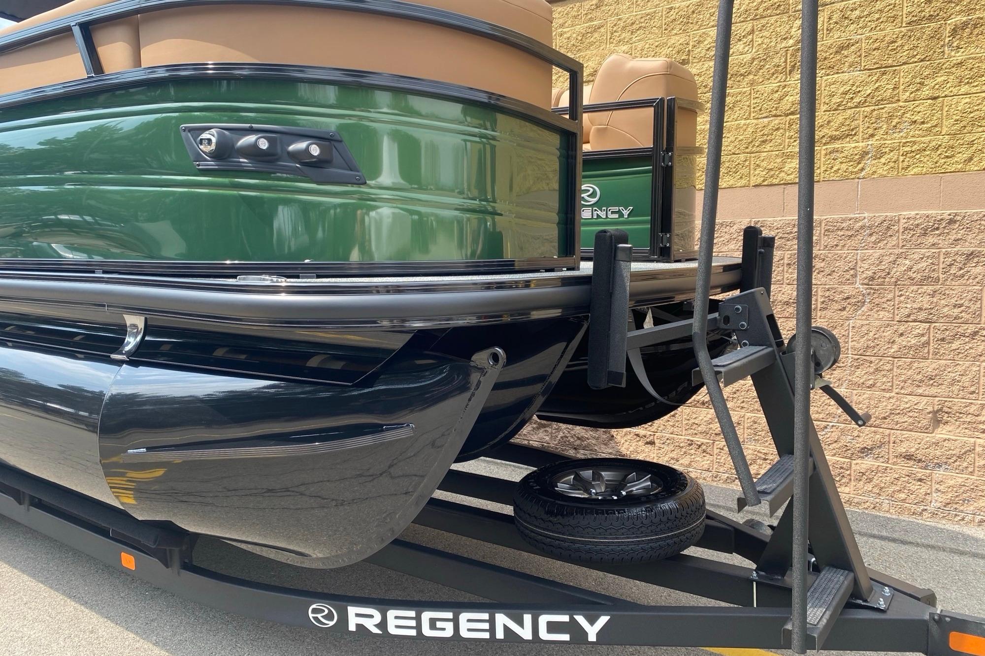 2026 Regency 230 DL boat on trailer, green exterior, parked by brick wall.