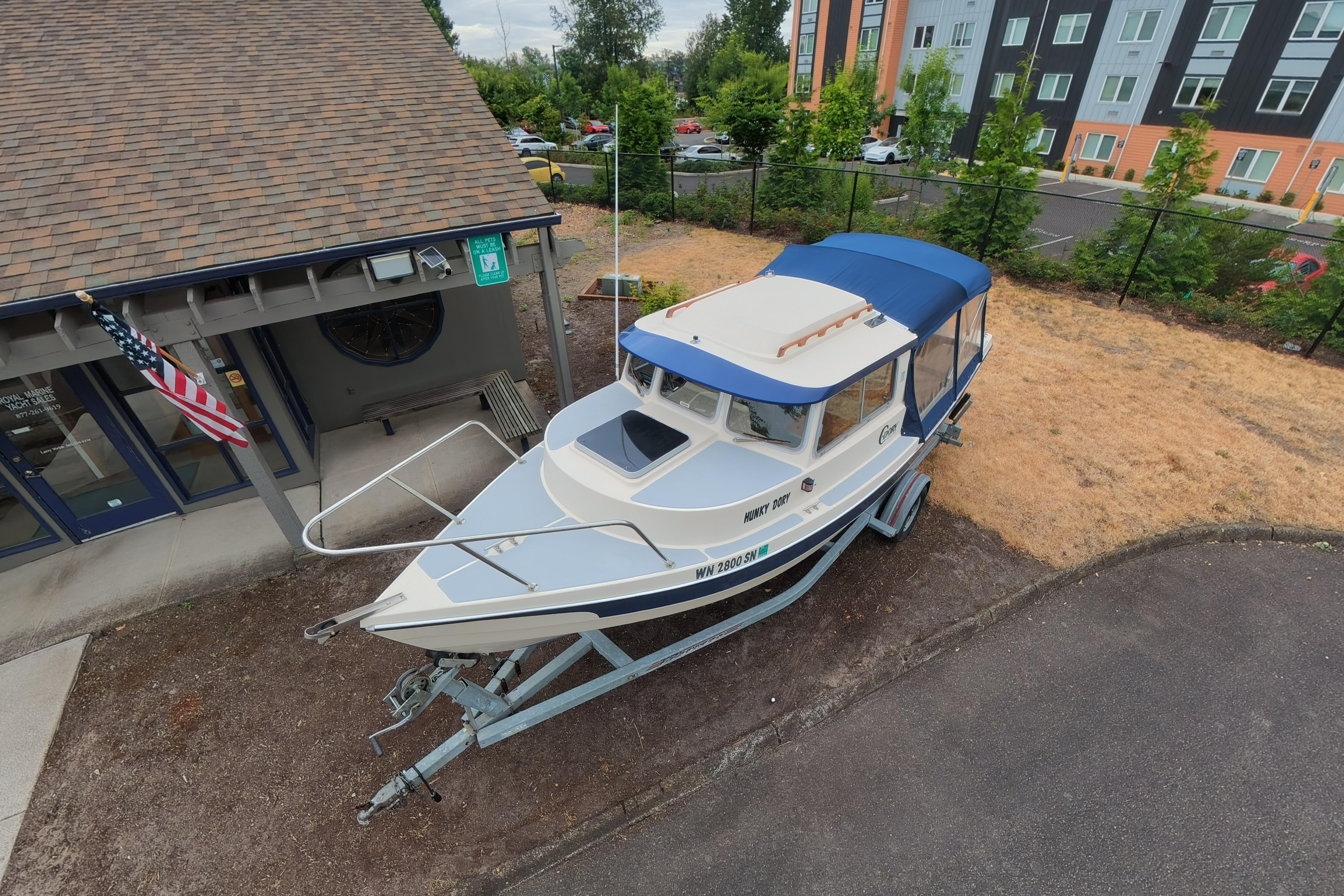 1989 C-Dory 22' Angler boat on trailer, parked near a building with an American flag.