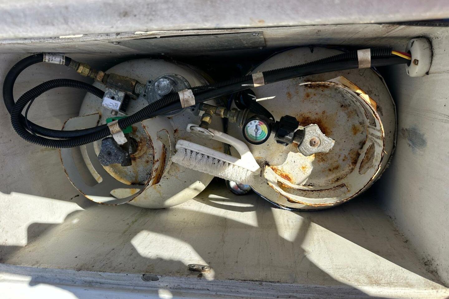 Two rusted propane tanks with gauges and hoses in a storage compartment.