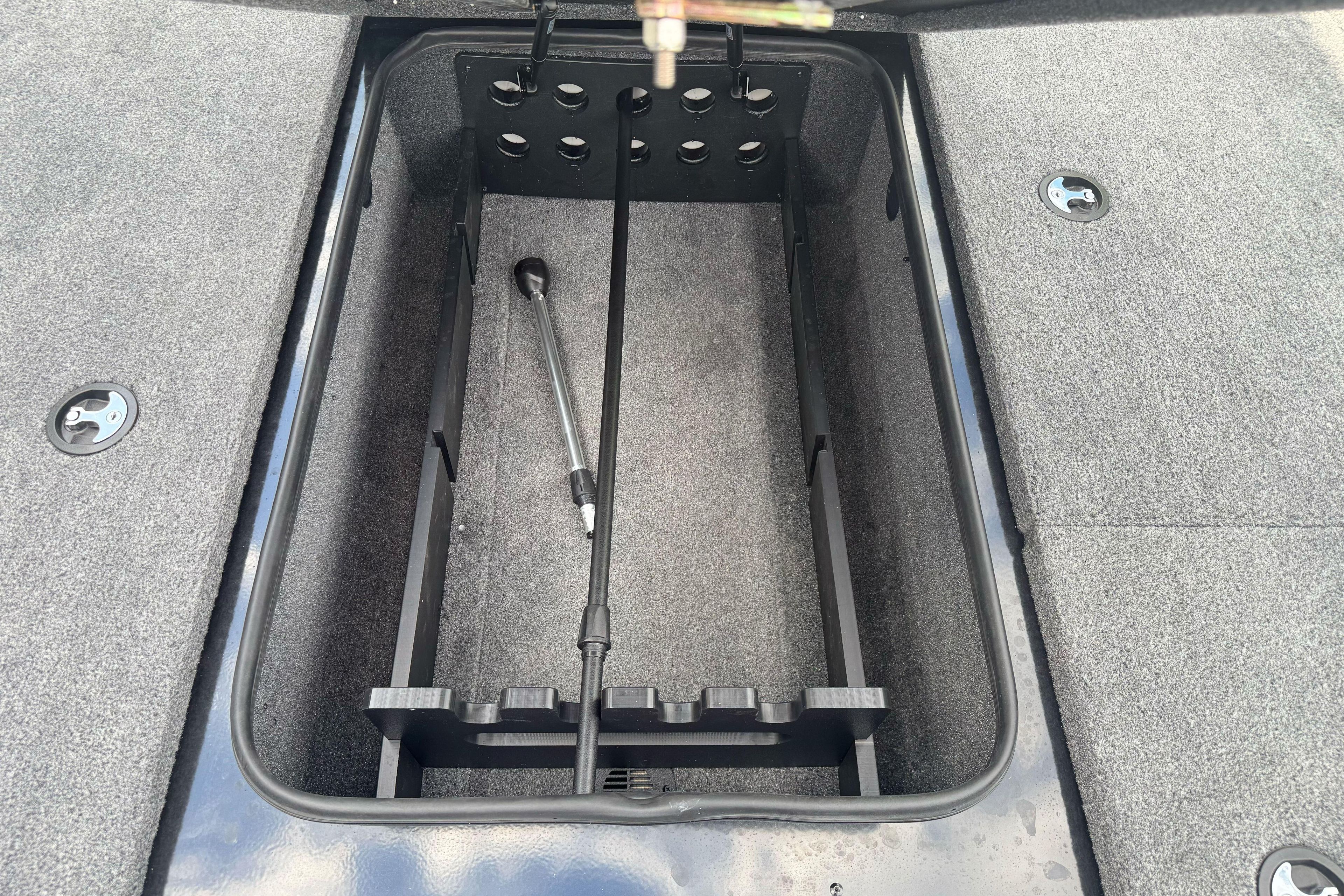 Open storage compartment in 2026 Ranger ALPHA 208 boat, featuring carpeted interior and rod holder.