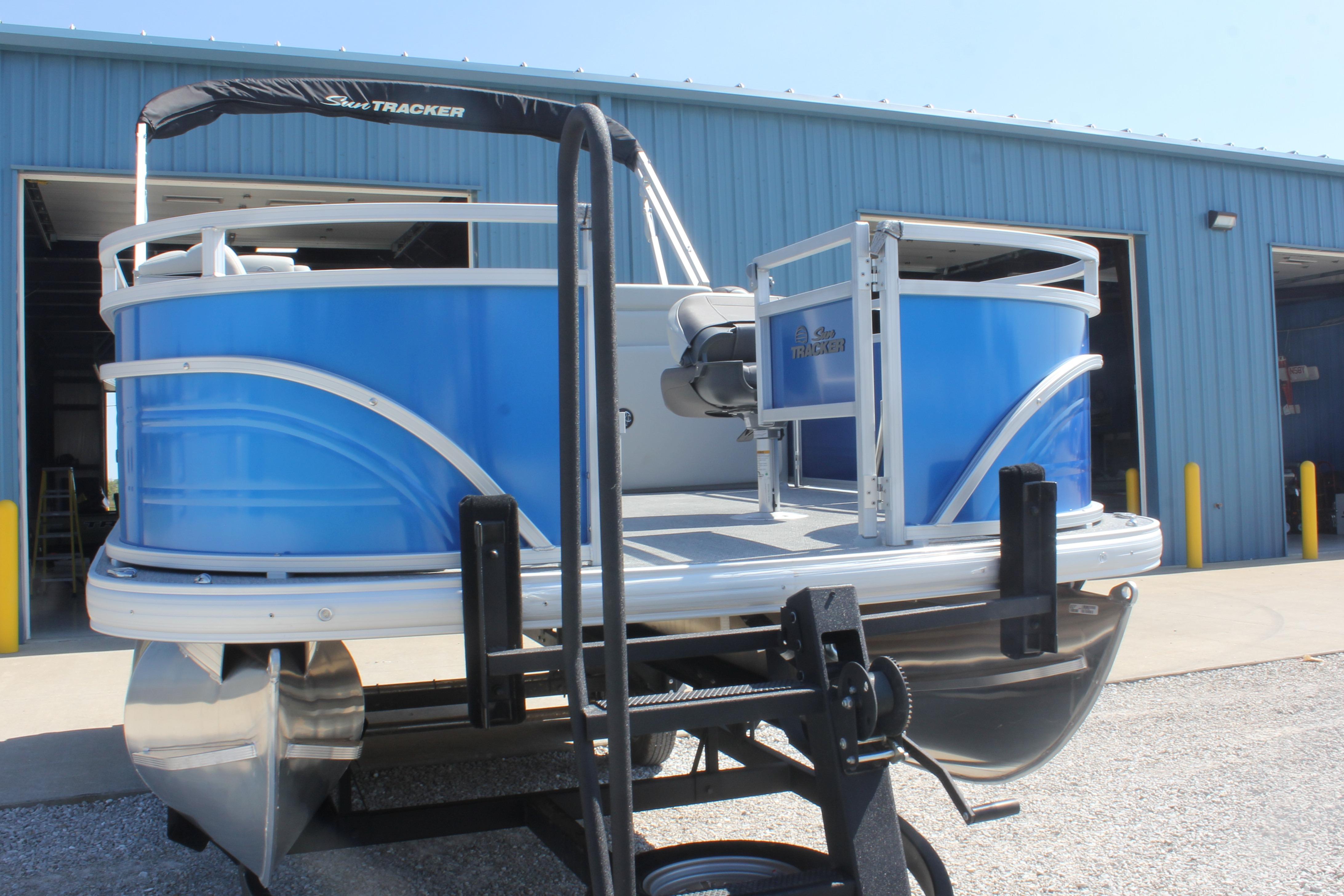 2026 Sun Tracker Fishin' Barge 20 DLX pontoon boat in front of a blue warehouse.