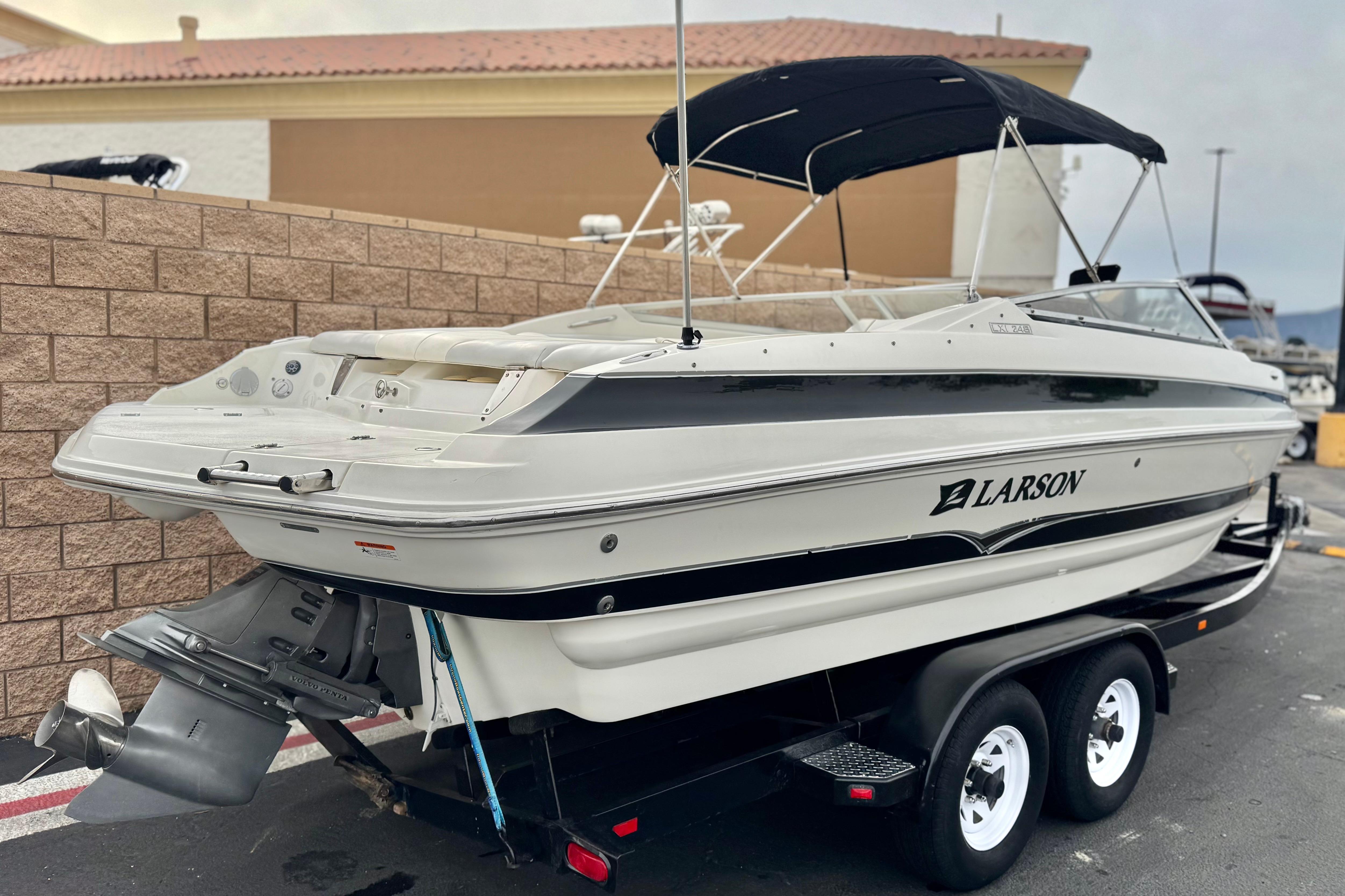 2006 Larson LXi 248 boat on trailer with black canopy, parked outdoors.