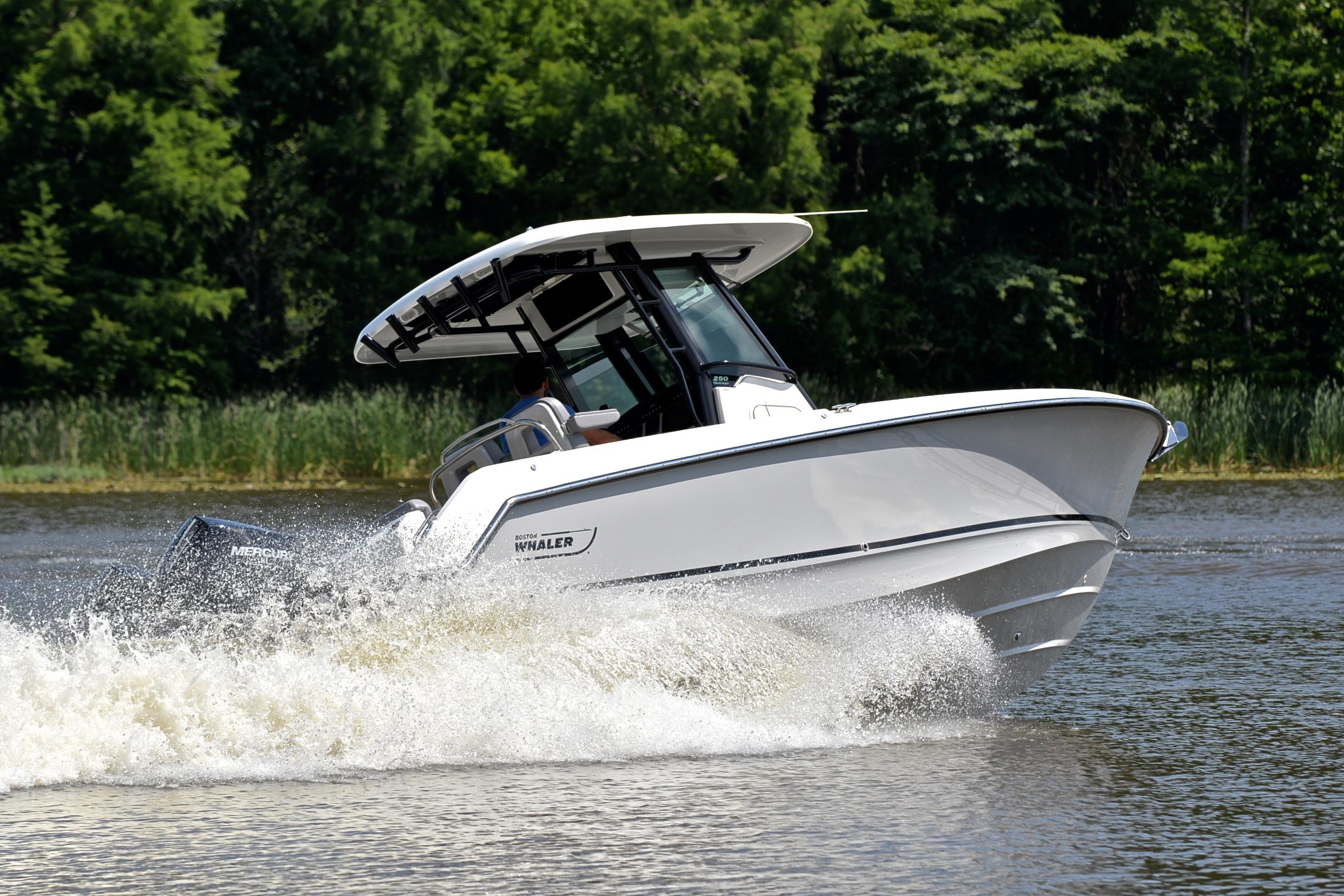 2024 Boston Whaler 250 Outrage cruising on a lake with lush green trees.