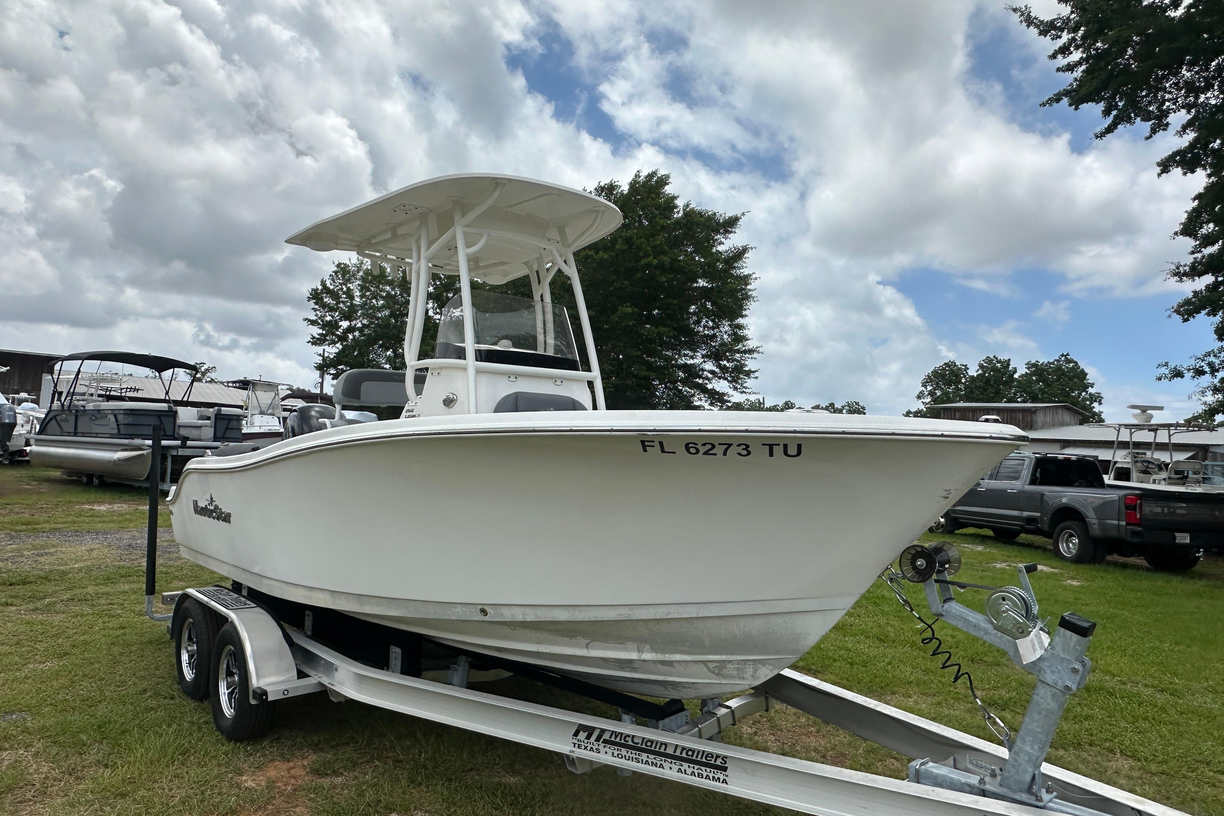 2023 NauticStar 2102 Legacy boat on trailer, parked outdoors under cloudy sky.