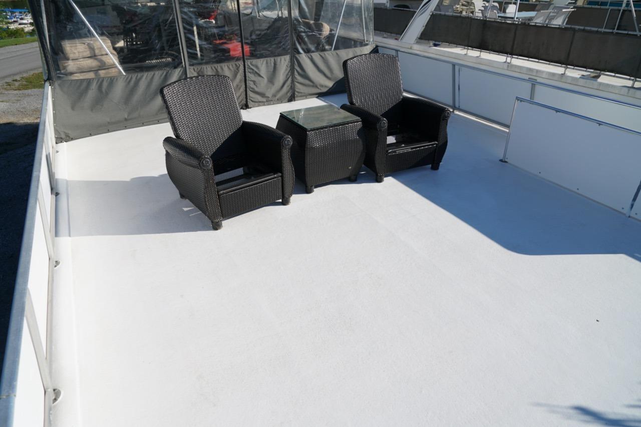 Upper deck of 2000 Stardust Cruisers houseboat with wicker chairs and glass table.