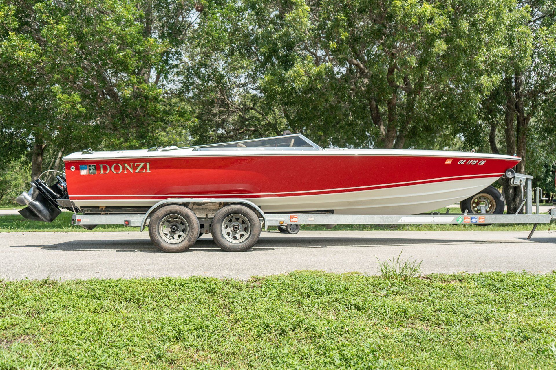 A red 1995 Donzi Classic boat on a trailer, set against a backdrop of trees.