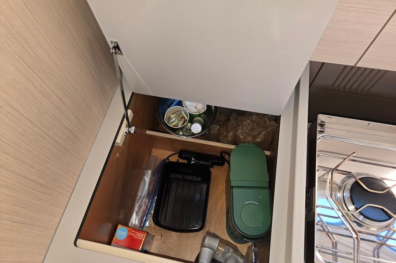Storage compartment in 2023 Beneteau Oceanis 38.1 yacht kitchen with various items.