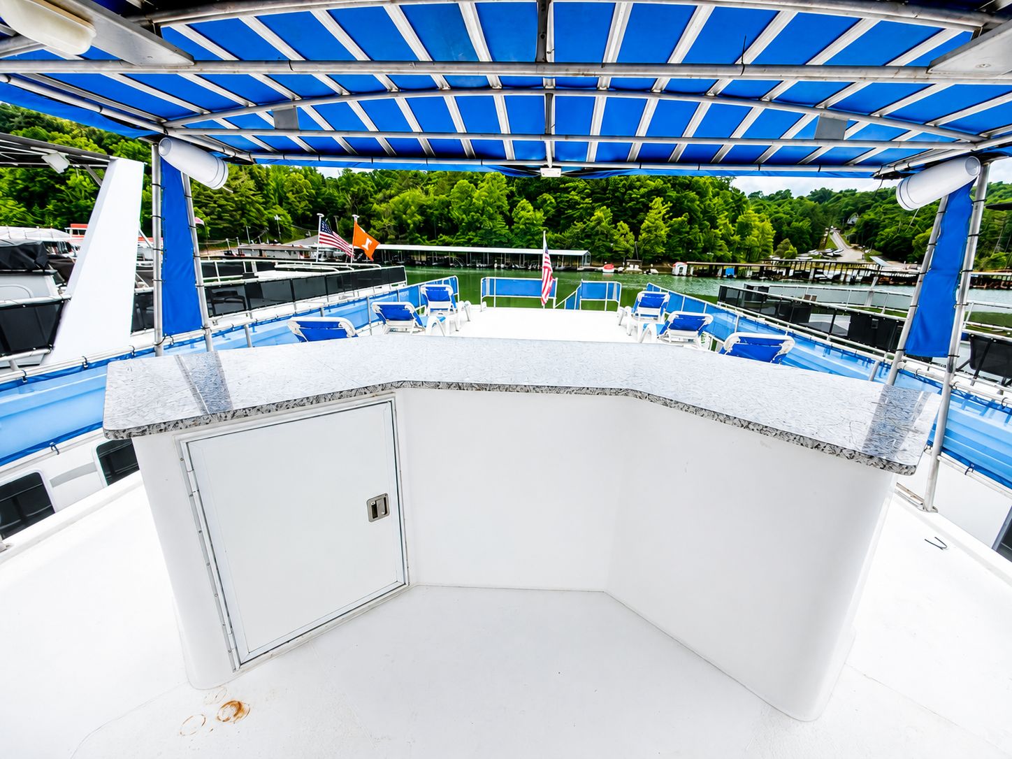 The image shows a houseboat deck with blue chairs and a blue sunshade.