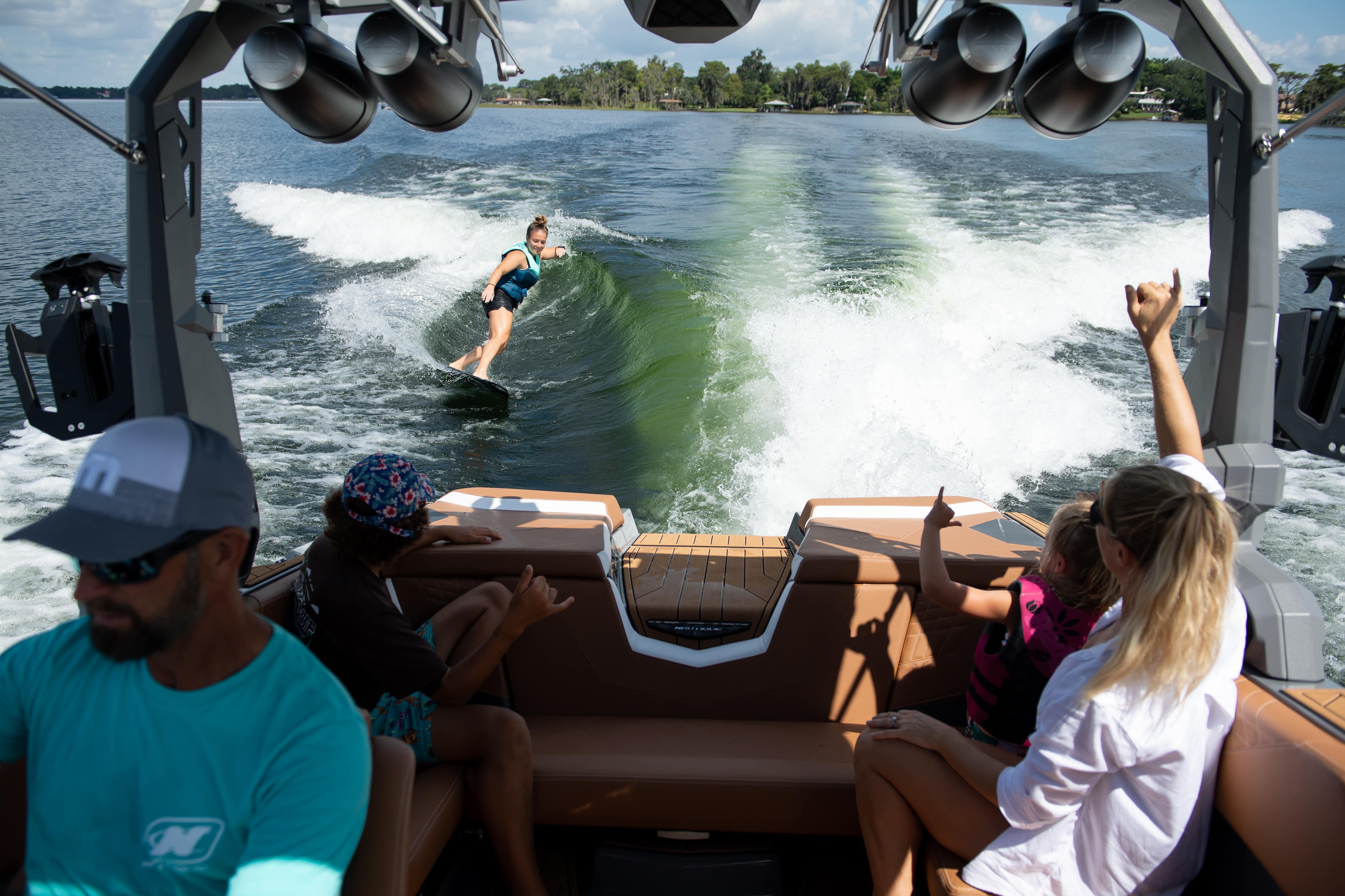 A Nautique S21 MY2026 boat with people enjoying wake surfing on a sunny day.