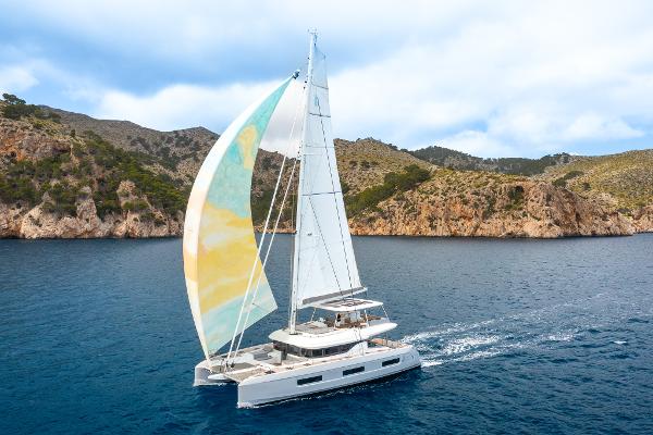 2025 Lagoon 60 yacht sailing near rocky coastline under clear skies.