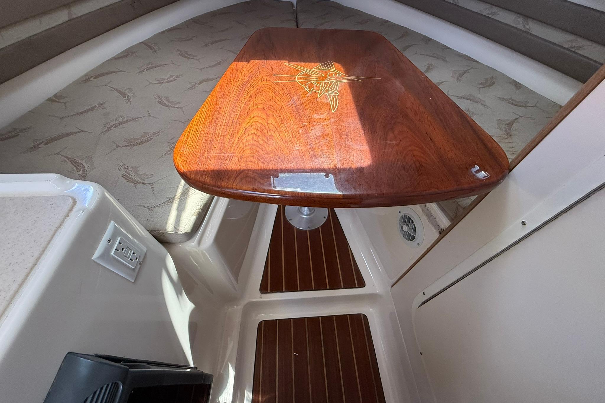 2003 Pursuit 2870 Walkaround cabin interior with wooden table and cushioned seating.