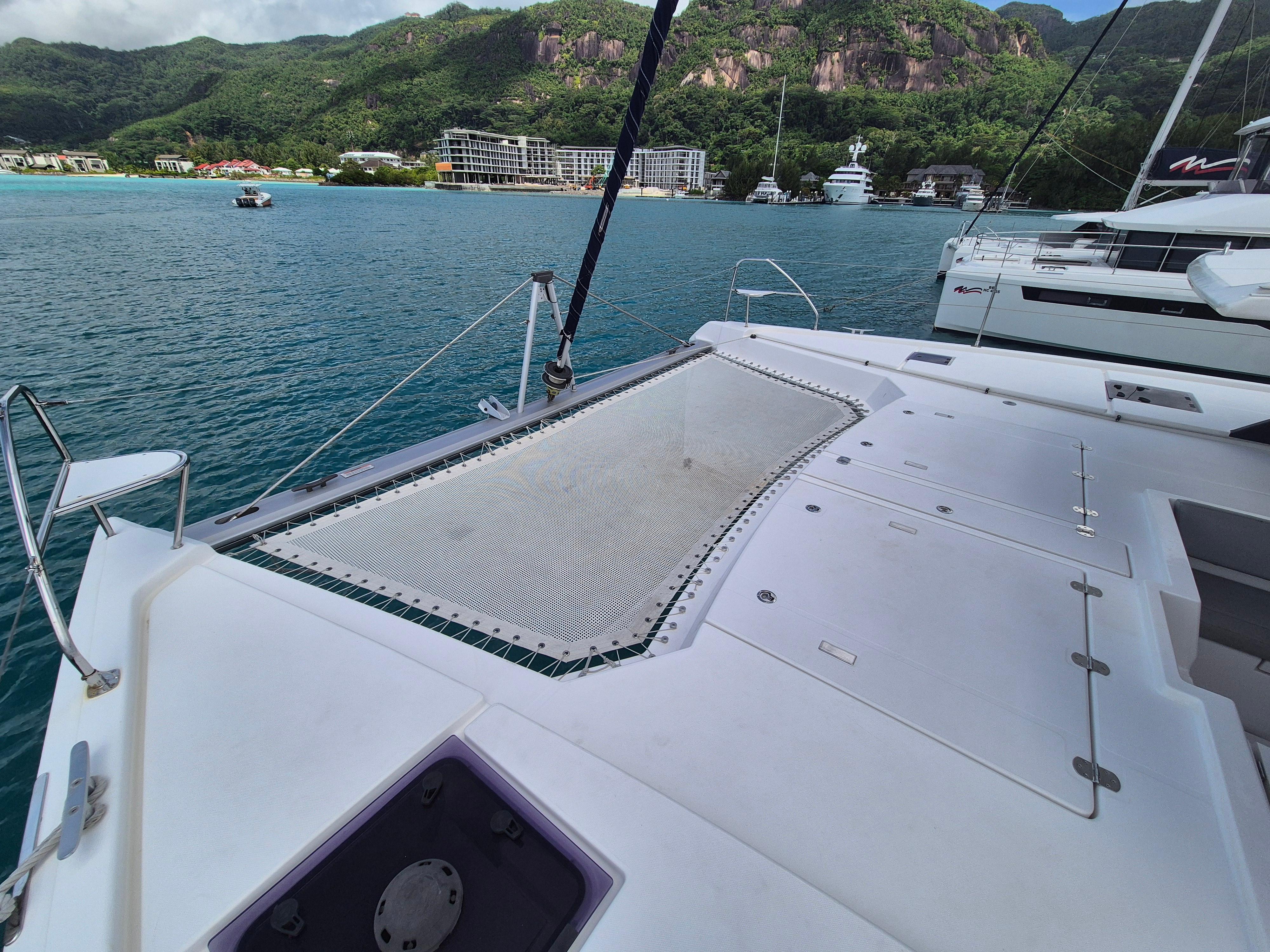 Catamaran deck with netting, Leopard 50, 2020 model, anchored near lush coastal landscape.