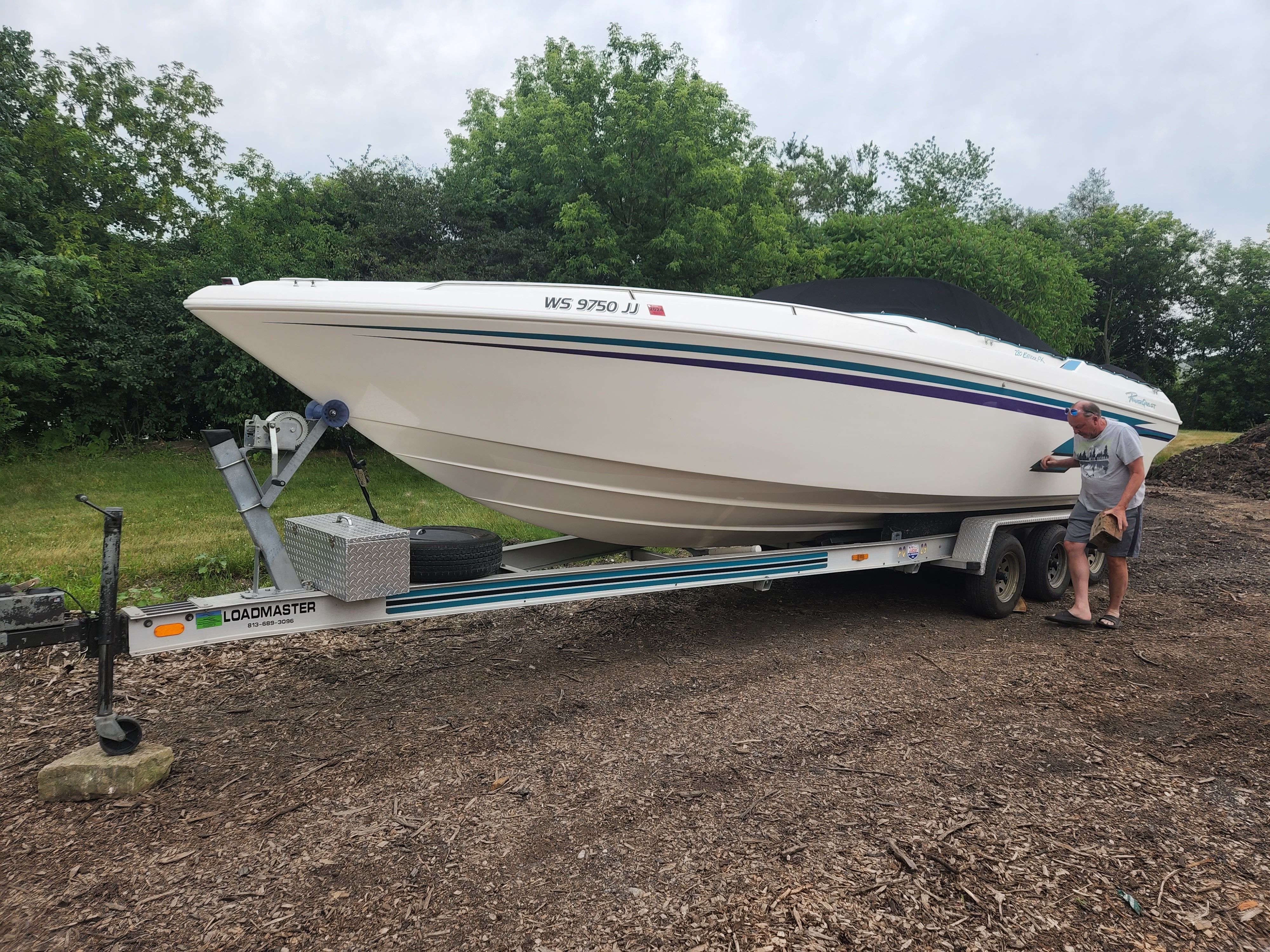 A white 1998 Powerquest Enticer 290 FX boat on a trailer, surrounded by trees.