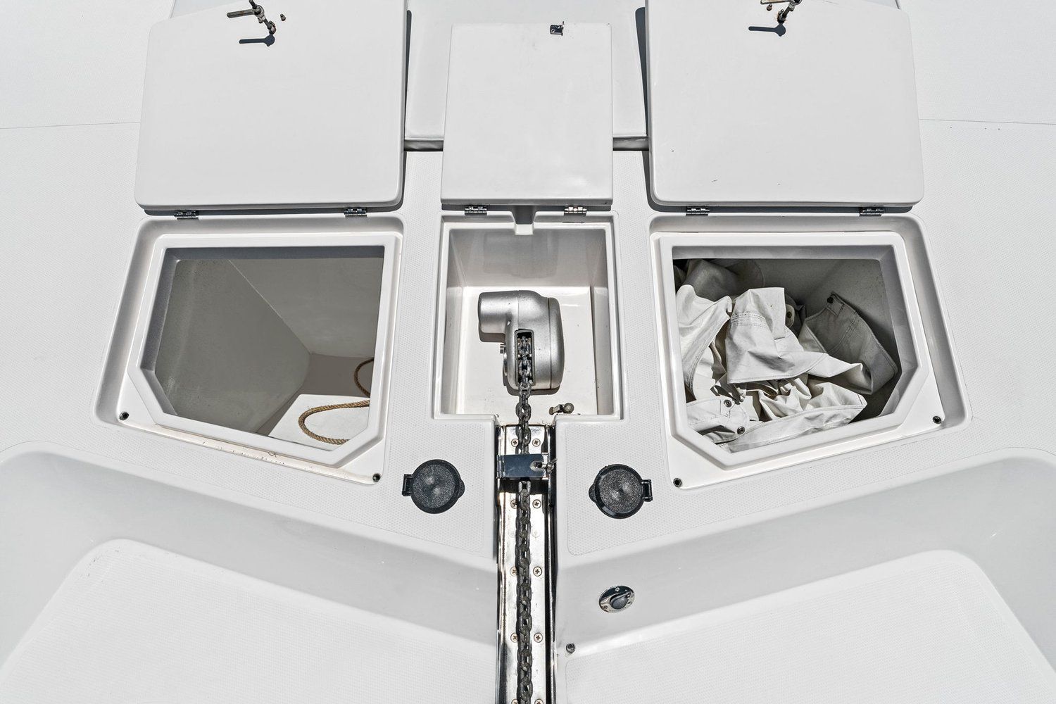 Deck of a catamaran with two storage compartments and an anchor windlass.