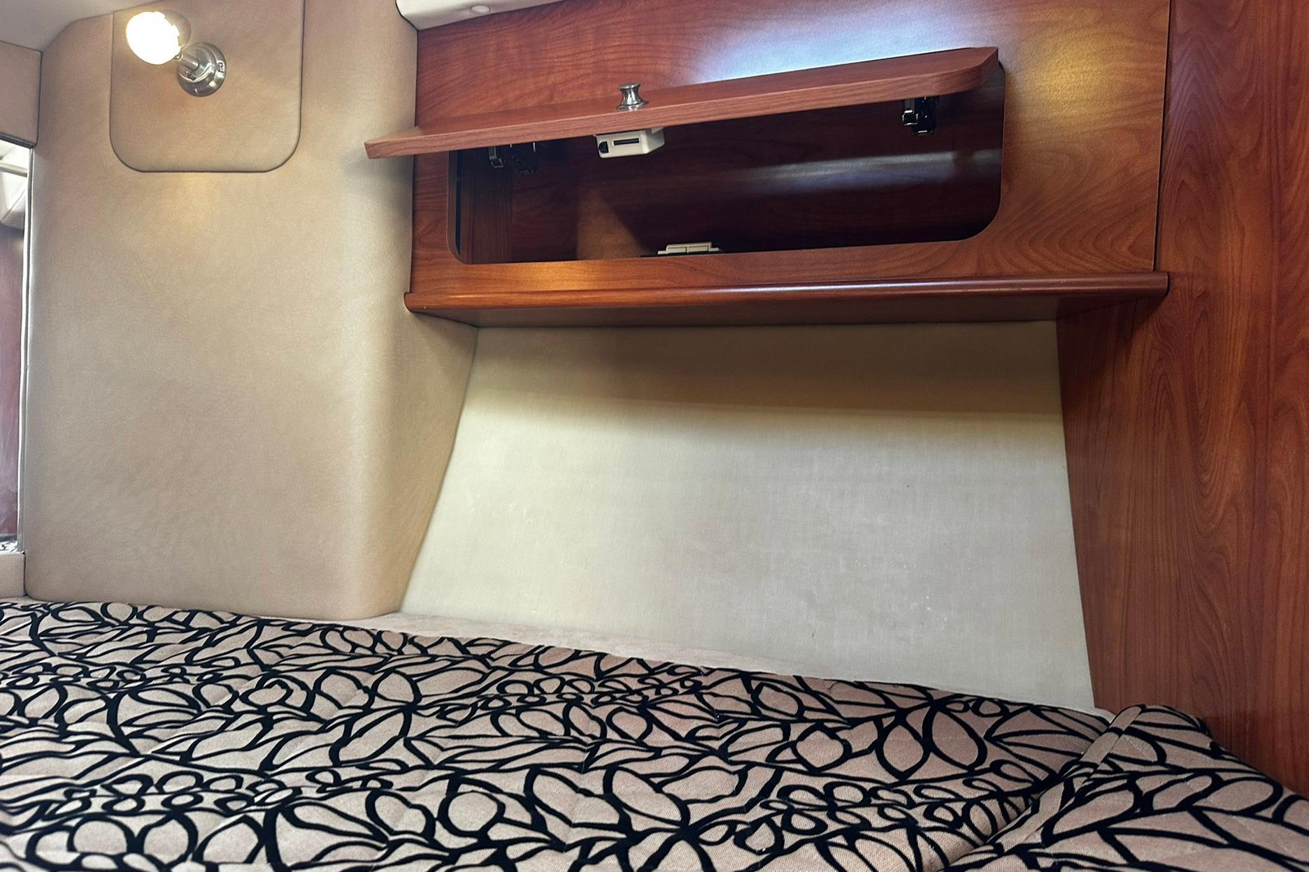 Interior cabin of 2012 Rinker 310 Express Cruiser LE with patterned bedding and wooden storage.
