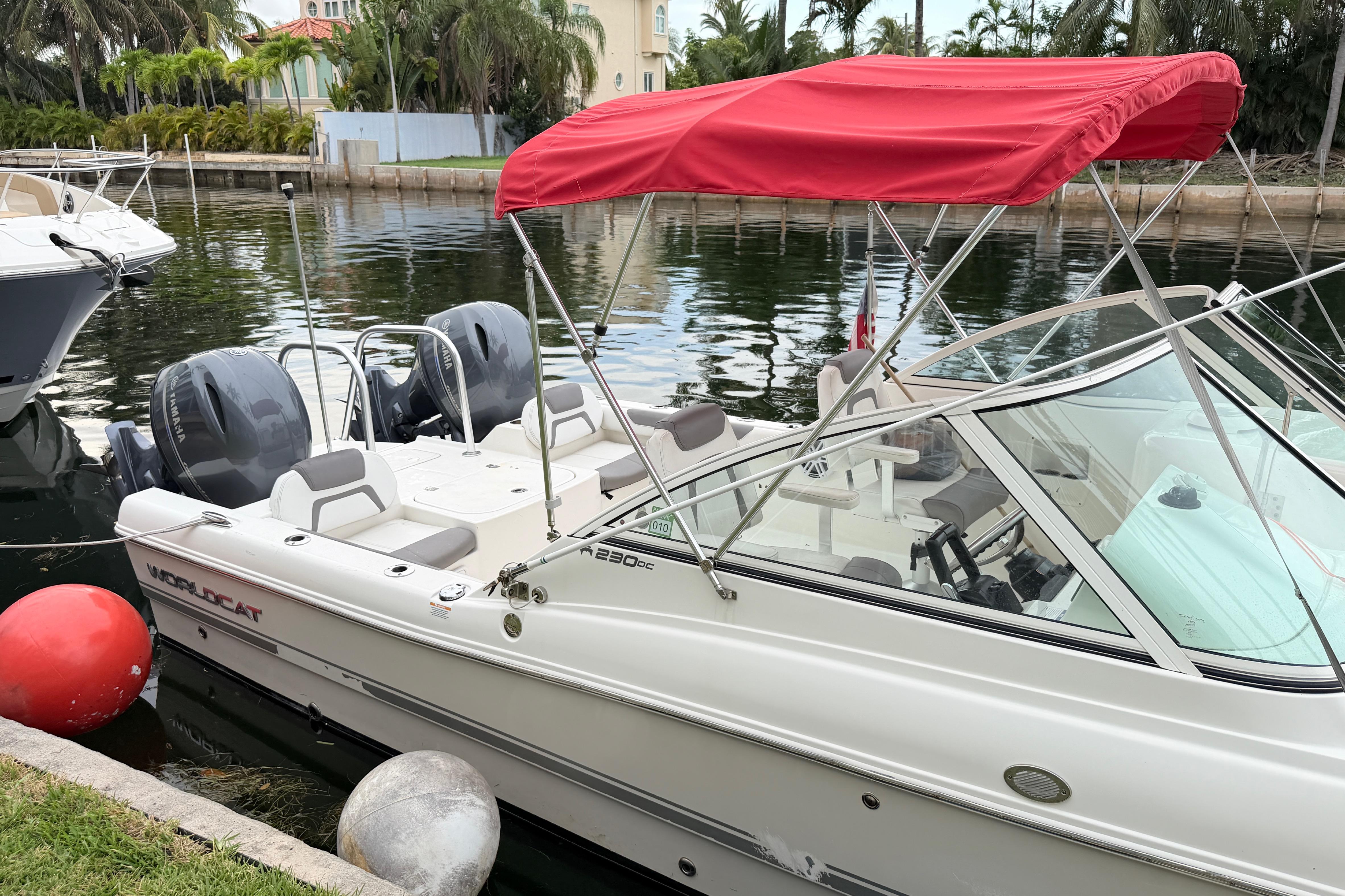 2019 World Cat 230 DC boat with red canopy docked by waterfront.