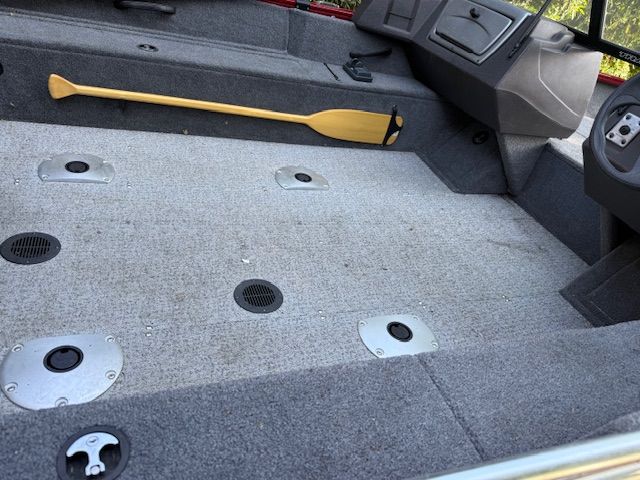 Interior of a Tracker PGV16WT 16 boat with gray carpet flooring and a yellow paddle.