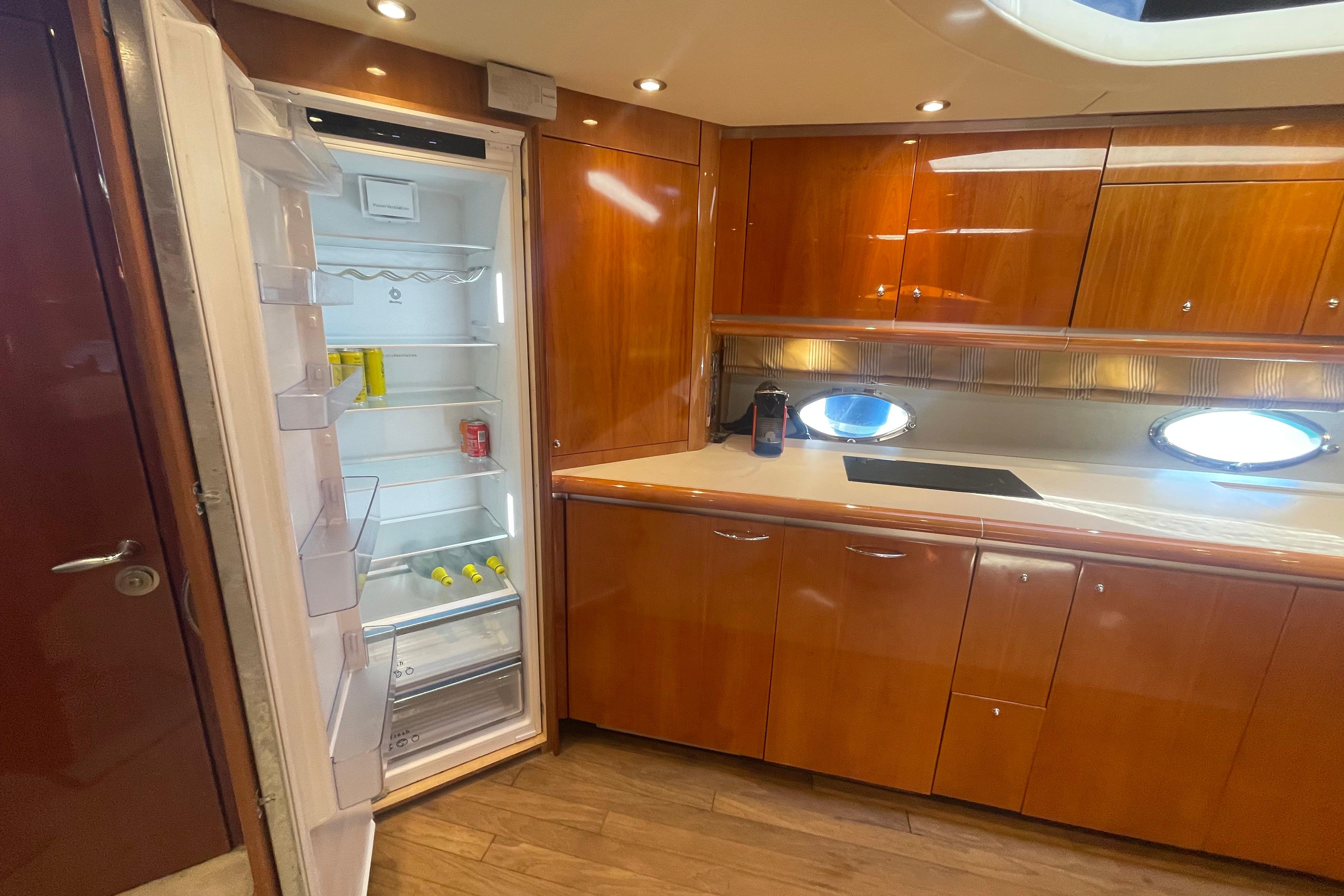 Luxurious 2003 Sunseeker Predator 68 yacht kitchen with open fridge and sleek wooden cabinetry.
