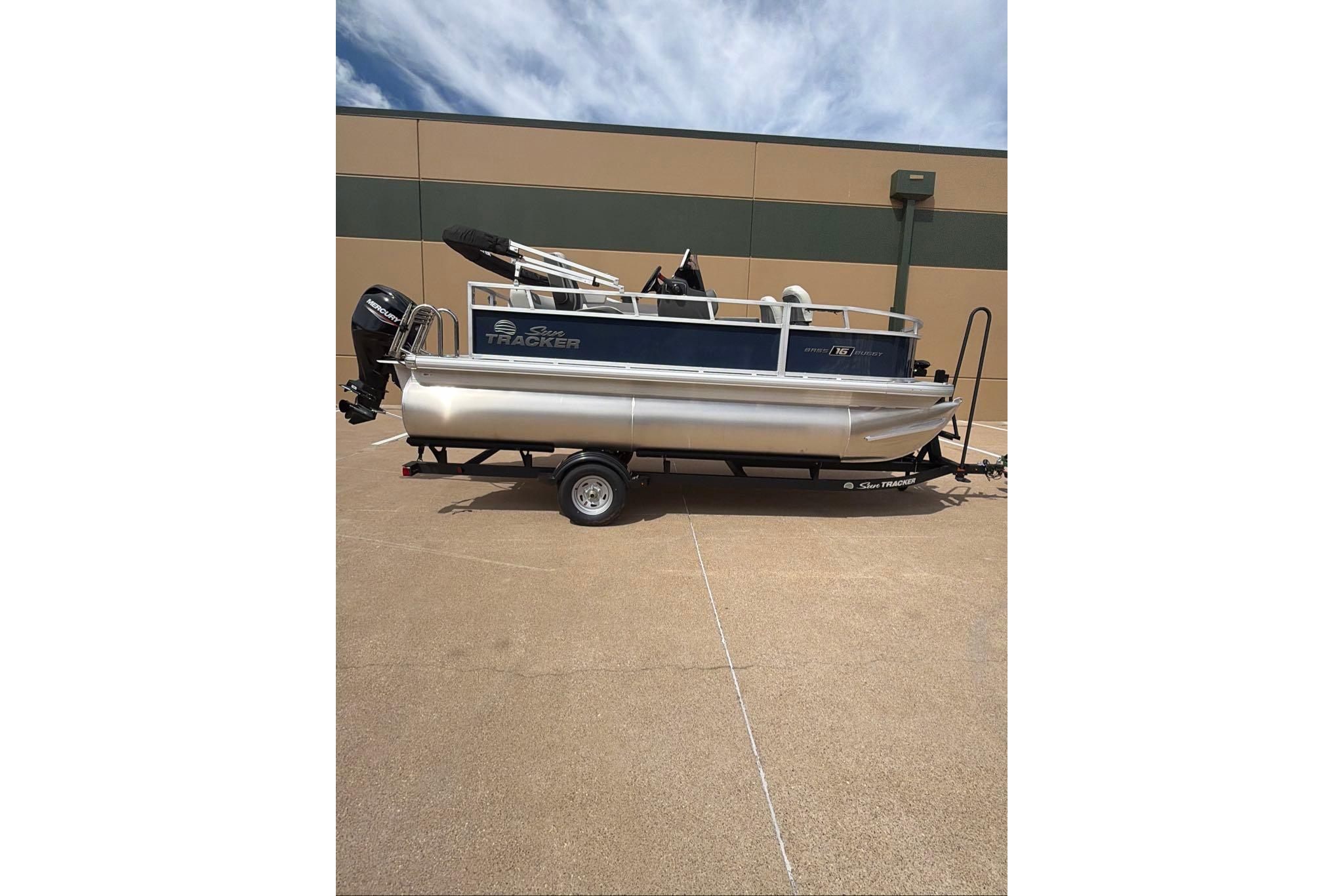 2026 Sun Tracker Bass Buggy 16 XL Select pontoon boat on trailer, parked outdoors.
