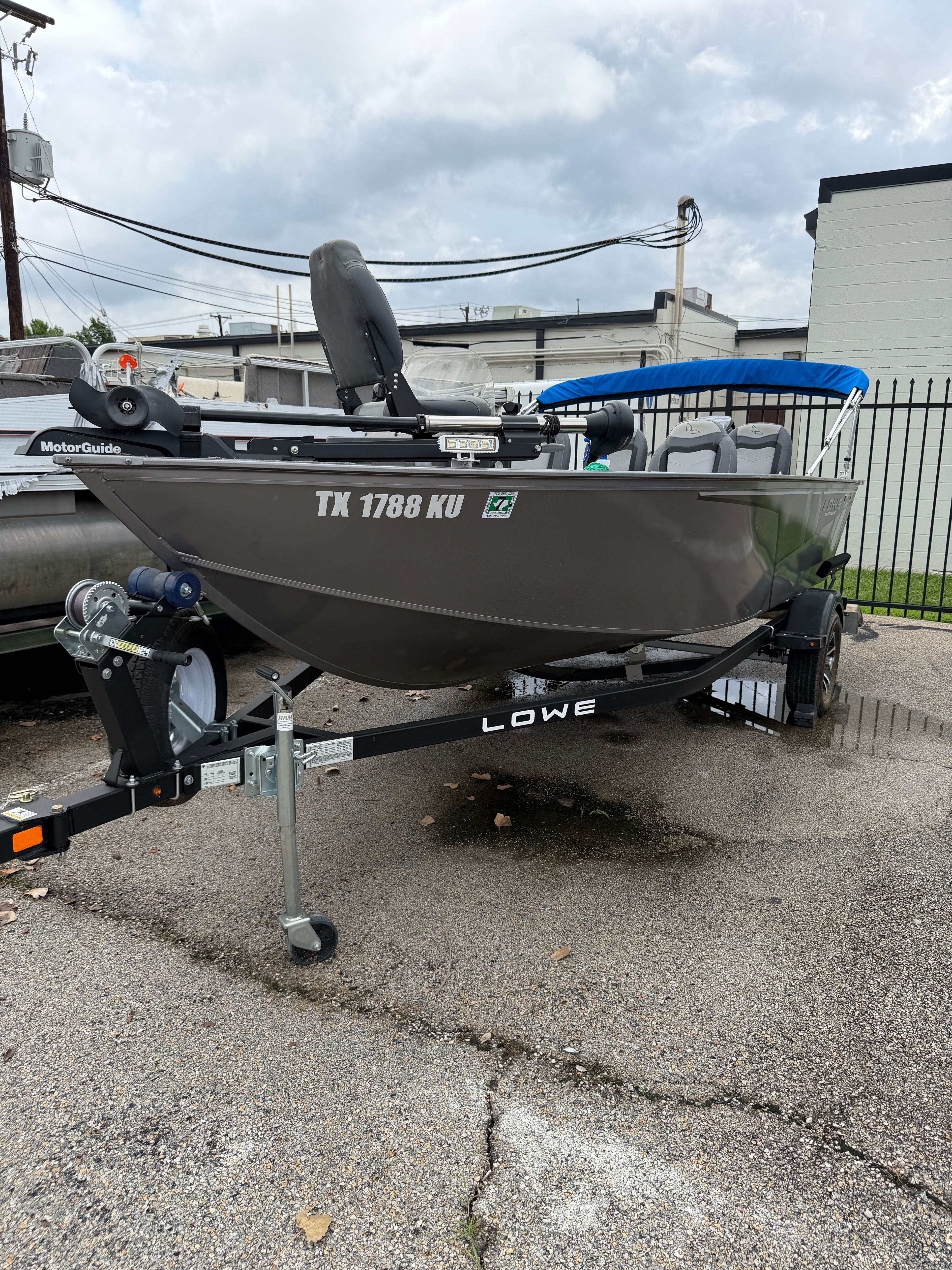 A gray 2023 Lowe Fishing Machine 1675SC boat on a trailer in a parking lot.