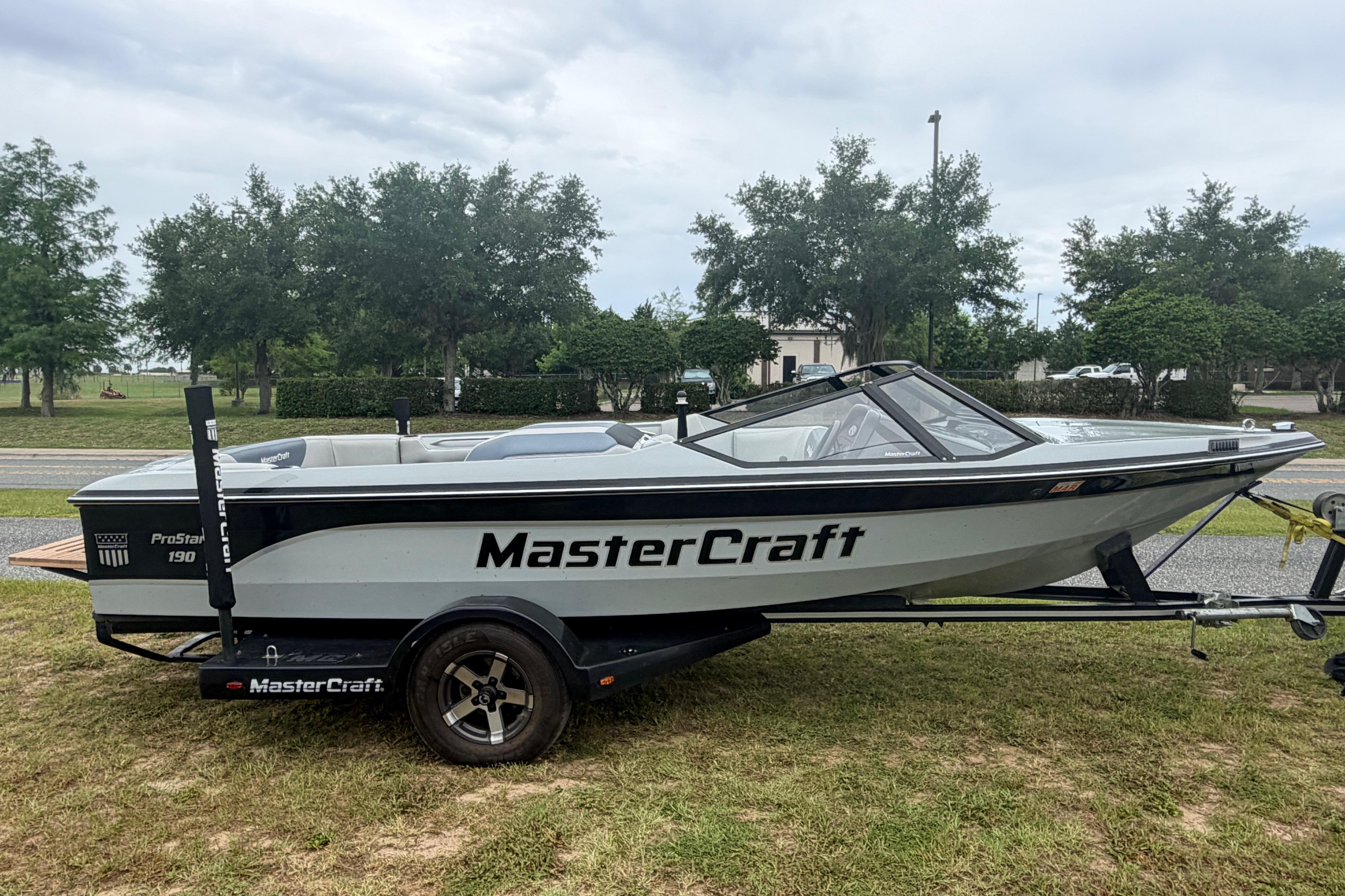 1989 MasterCraft ProStar 190 boat on trailer, parked on grass with trees in background.