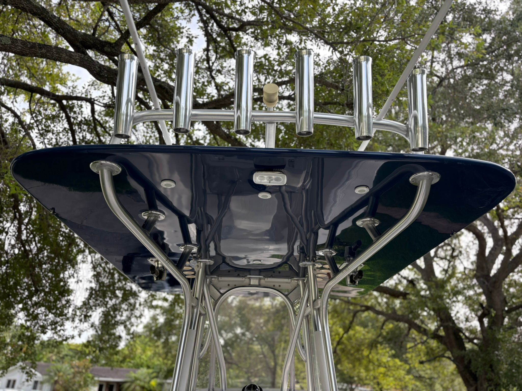 View of a boat's roof with multiple fishing rod holders and trees in the background.