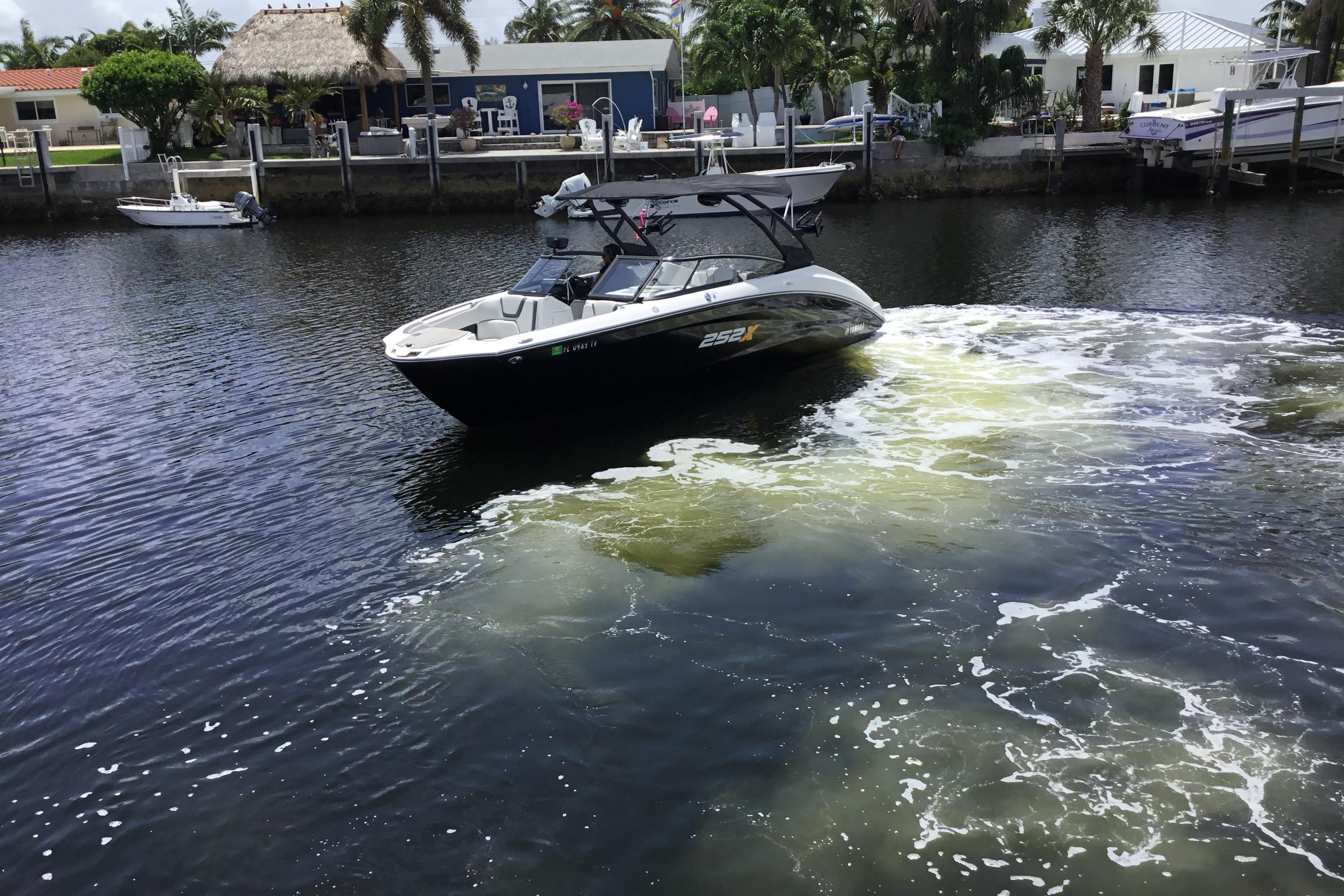 2023 Yamaha Boats 252XE cruising on a calm waterway near a residential area.