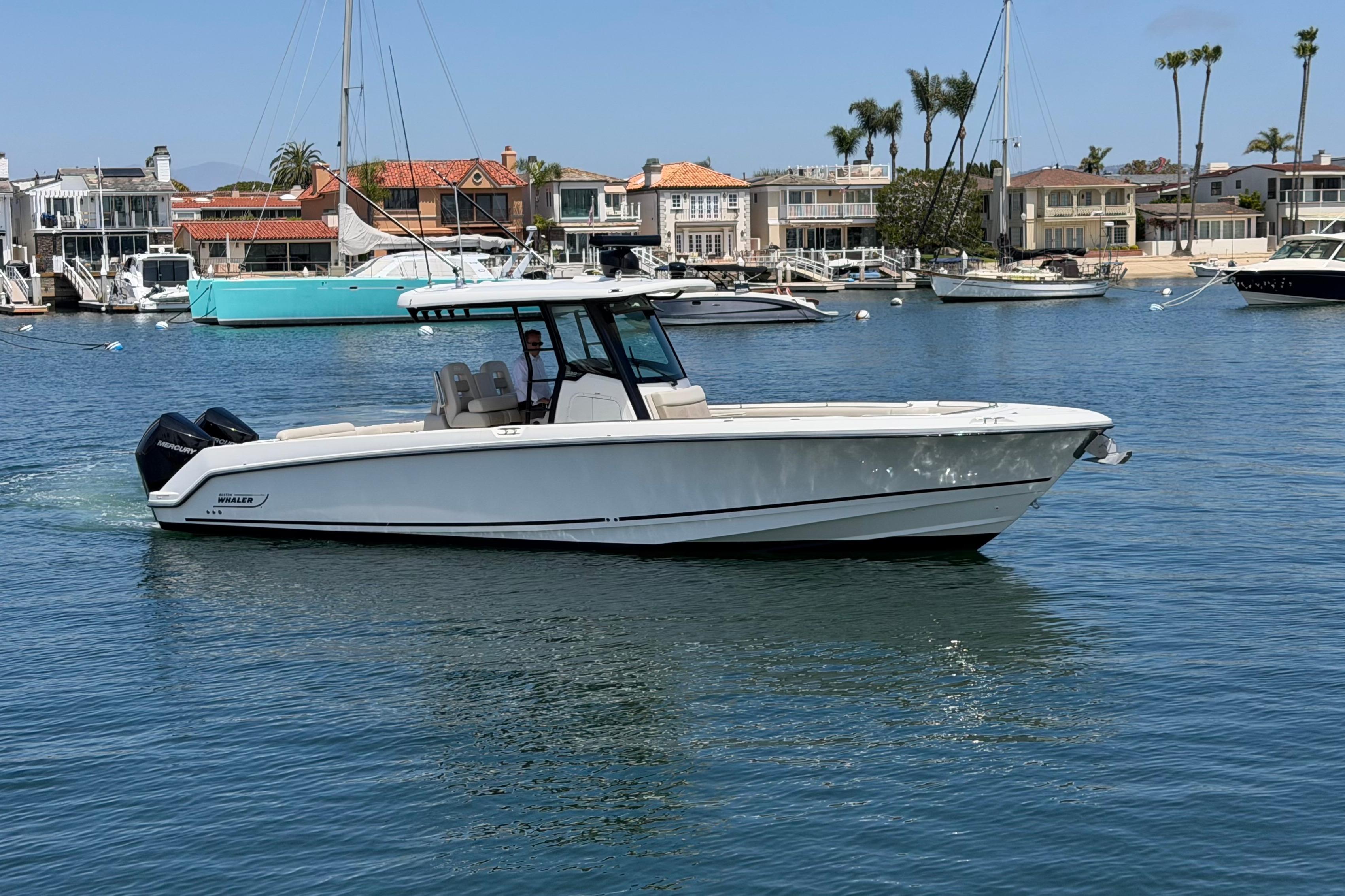 2021 Boston Whaler 330 Outrage boat cruising in a marina with waterfront homes.