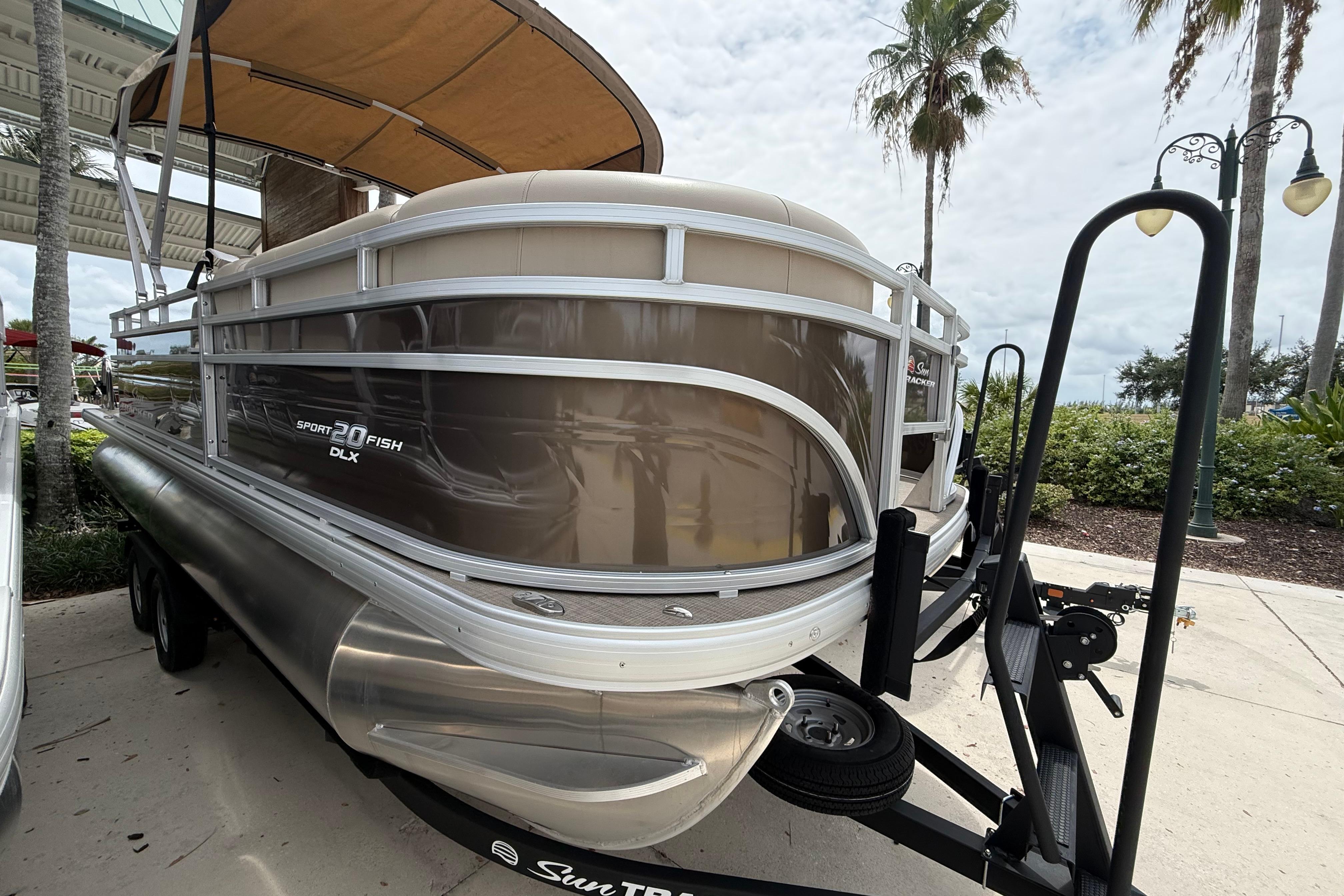 2025 Sun Tracker SportFish 20 DLX pontoon boat on trailer, parked outdoors.