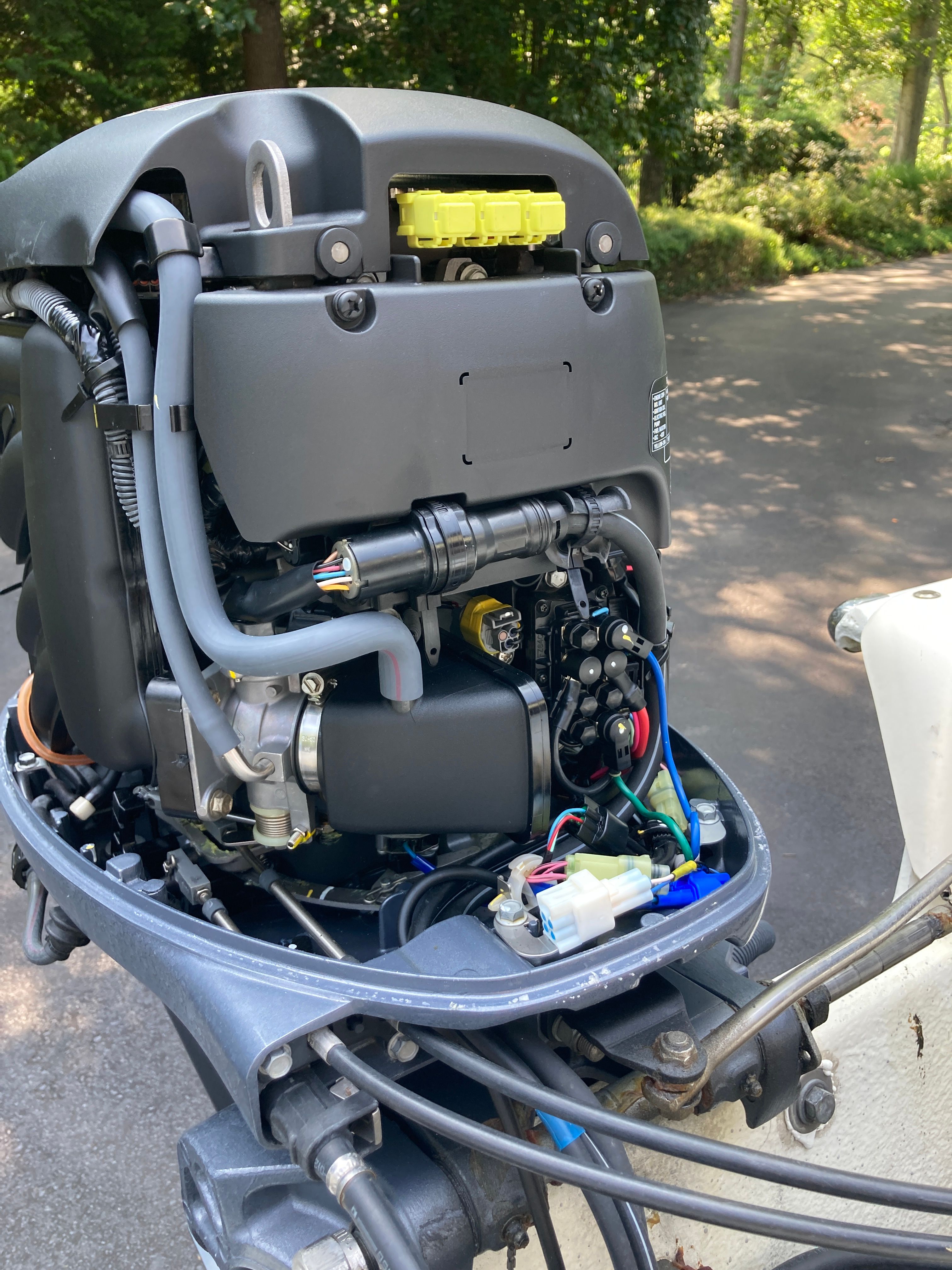 An outboard motor with exposed wires and components, surrounded by trees in the background.