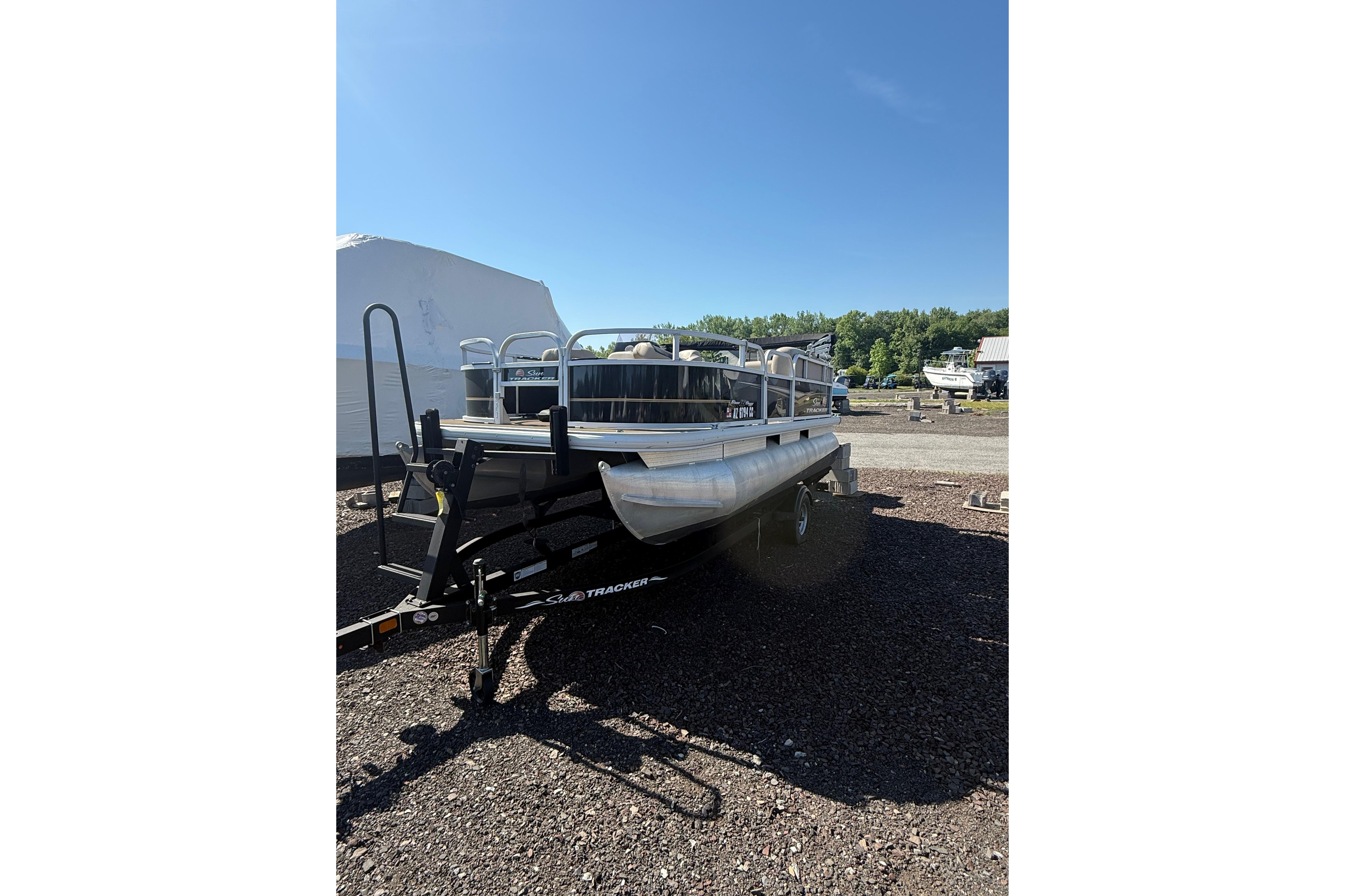 2021 Sun Tracker Bass Buggy 16 XL Select pontoon boat on trailer under clear blue sky.