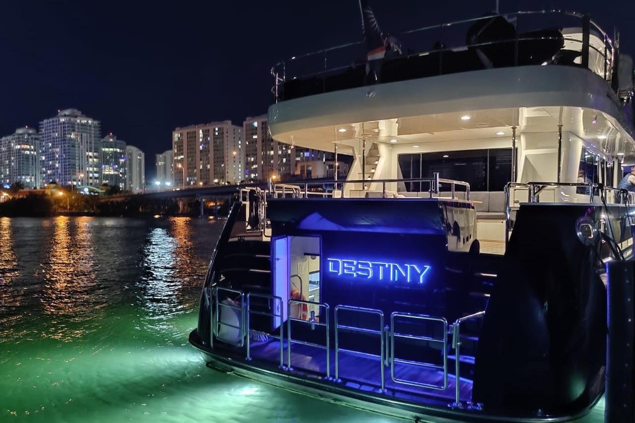 Luxurious Fifth Ocean Yachts 24m Explorer Yacht at night, city skyline in background.