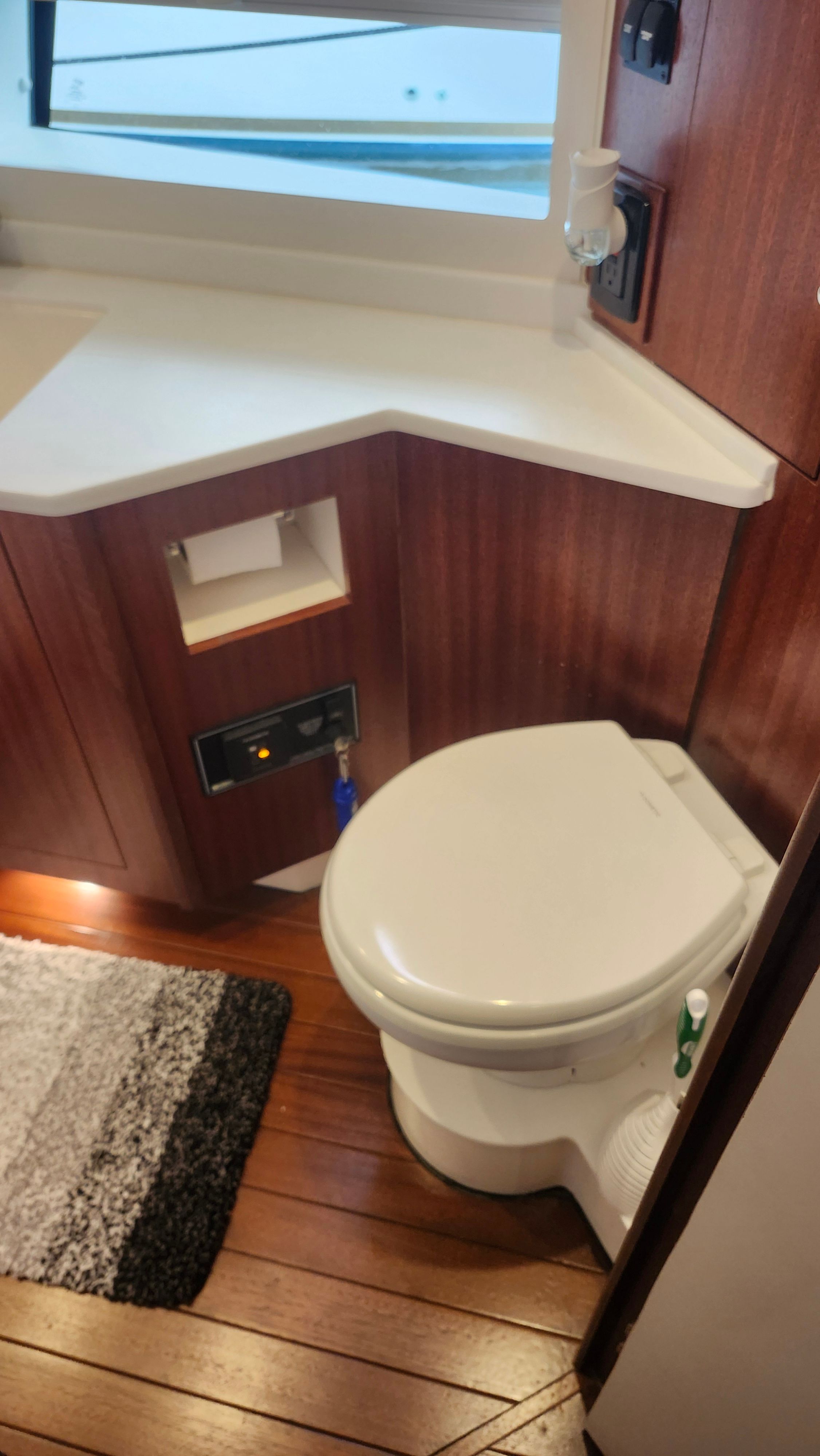 Interior view of a boat cabin with a toilet, wooden floor, and window.