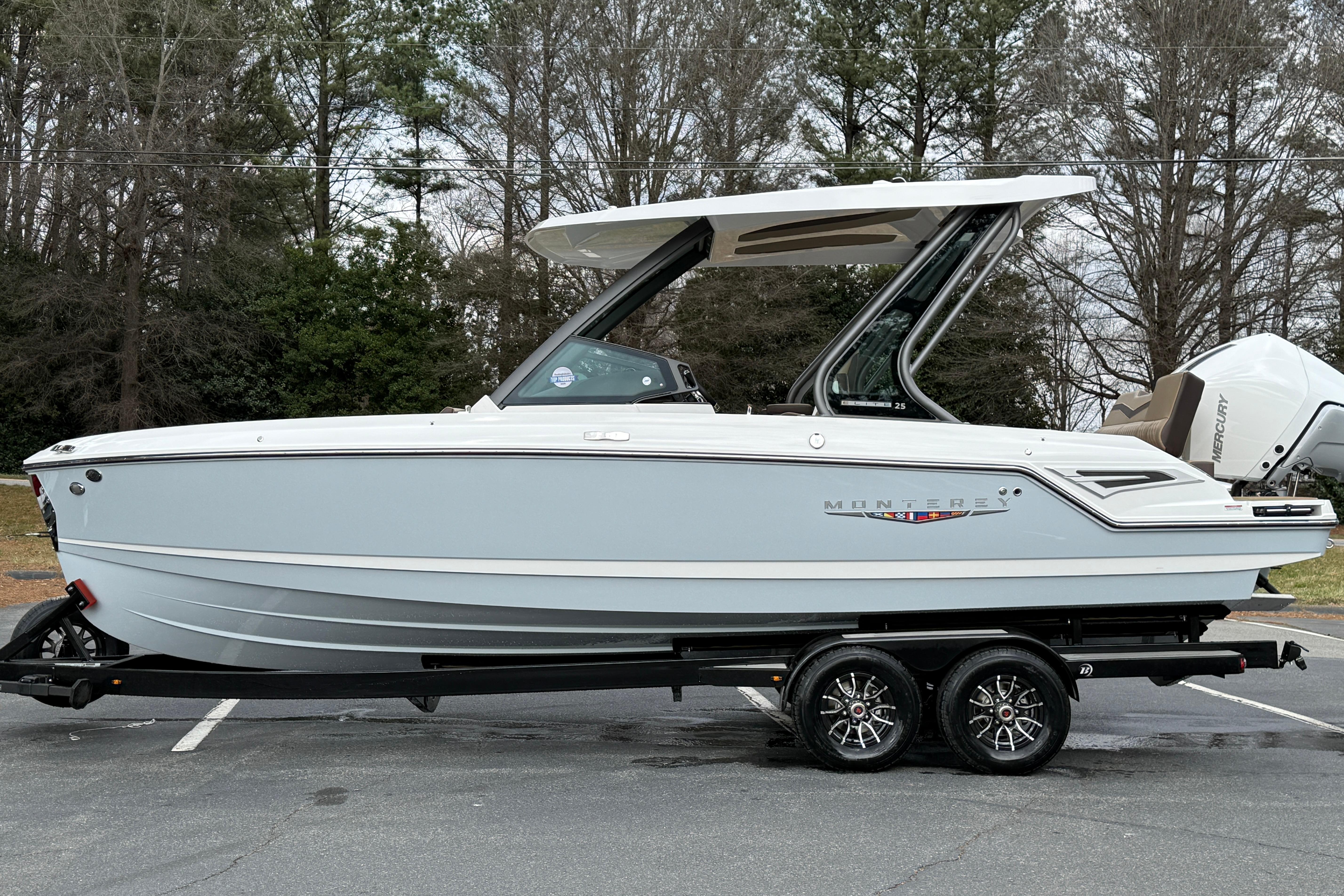 2026 Monterey Elite 25 OB boat on trailer, parked outdoors with trees in background.