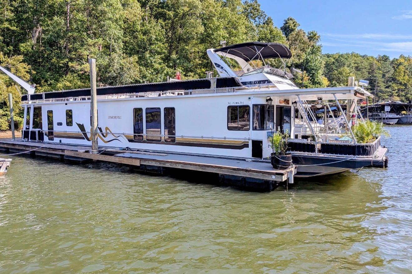 Houseboat docked on a lake, 1996 Stardust Cruisers 14.5 x 69 model, surrounded by trees.