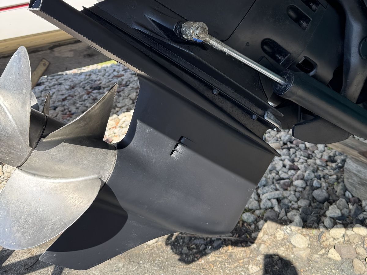 Close-up of a boat propeller and drive shaft on a gravel surface.