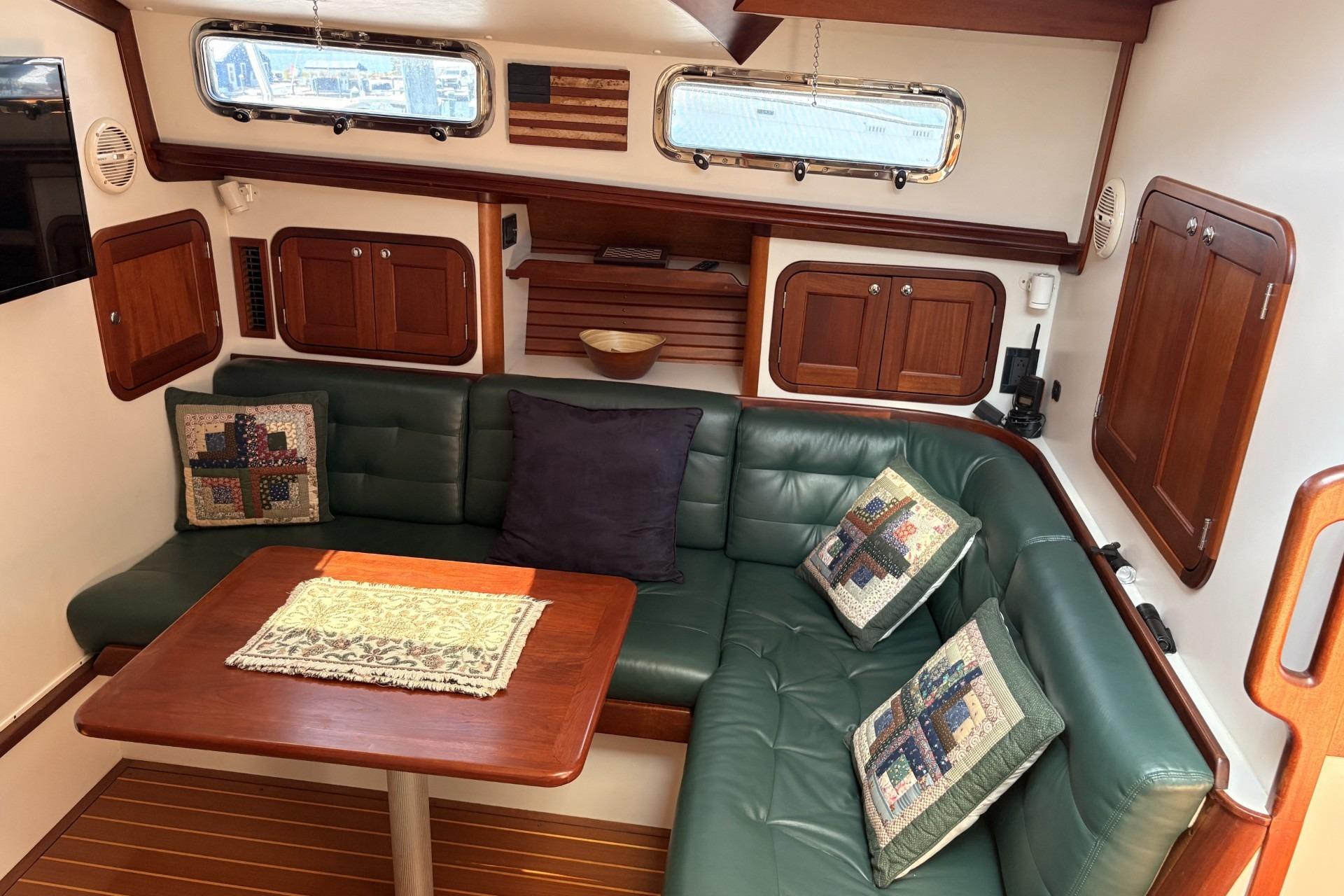 Cozy boat interior with green leather seating, wooden table, and decorative pillows.
