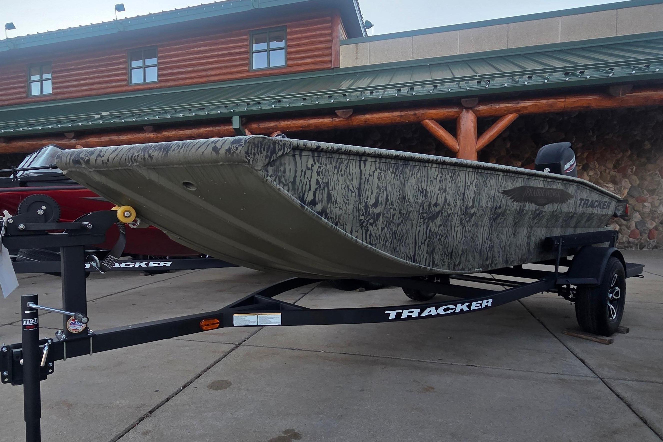 2026 Tracker Grizzly 1650 T Prairie Wings Edition boat on trailer outside a log building.