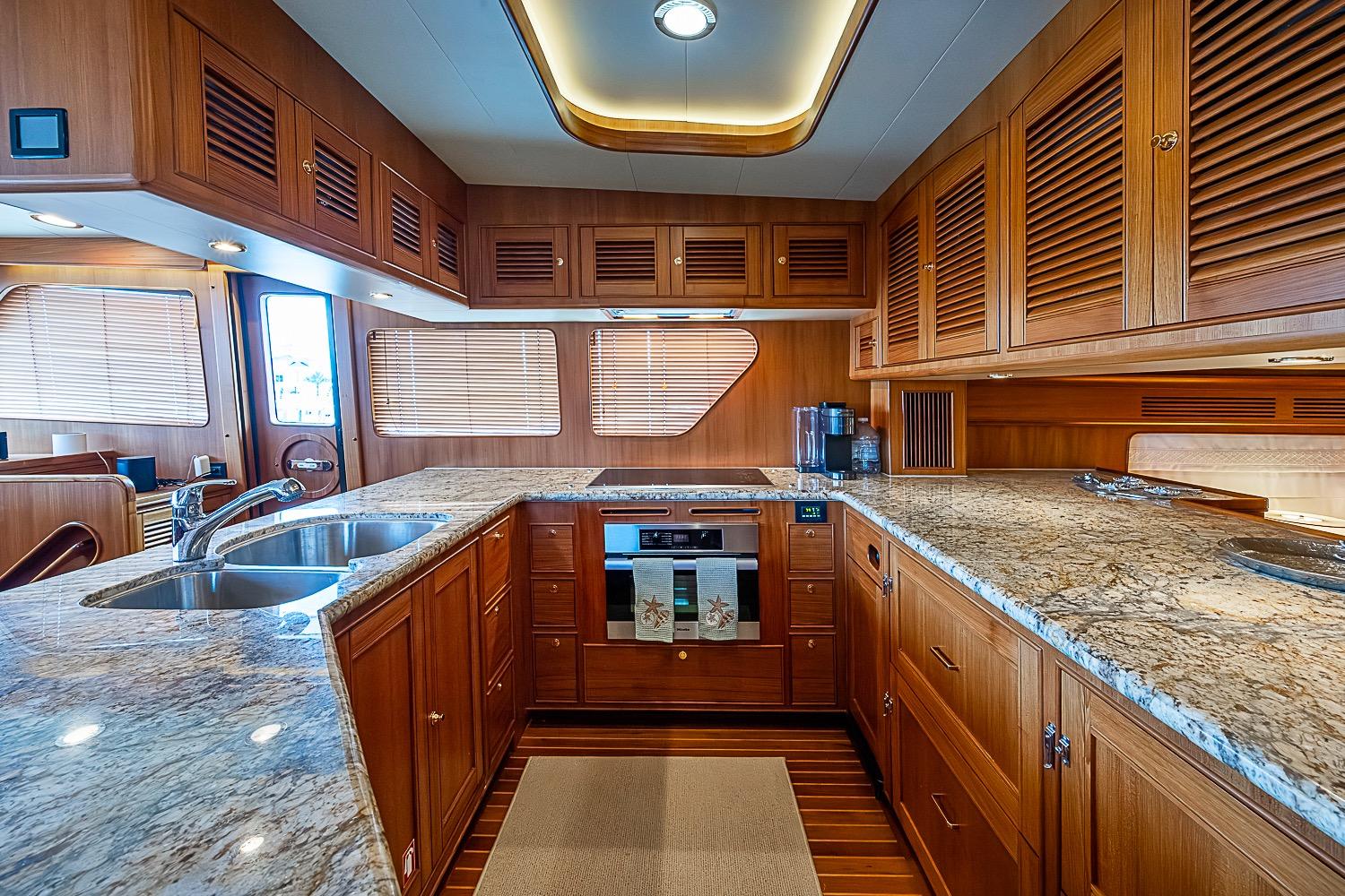 Luxurious kitchen interior of 2014 Marlow 80 Explorer yacht with wooden cabinetry and granite countertops.
