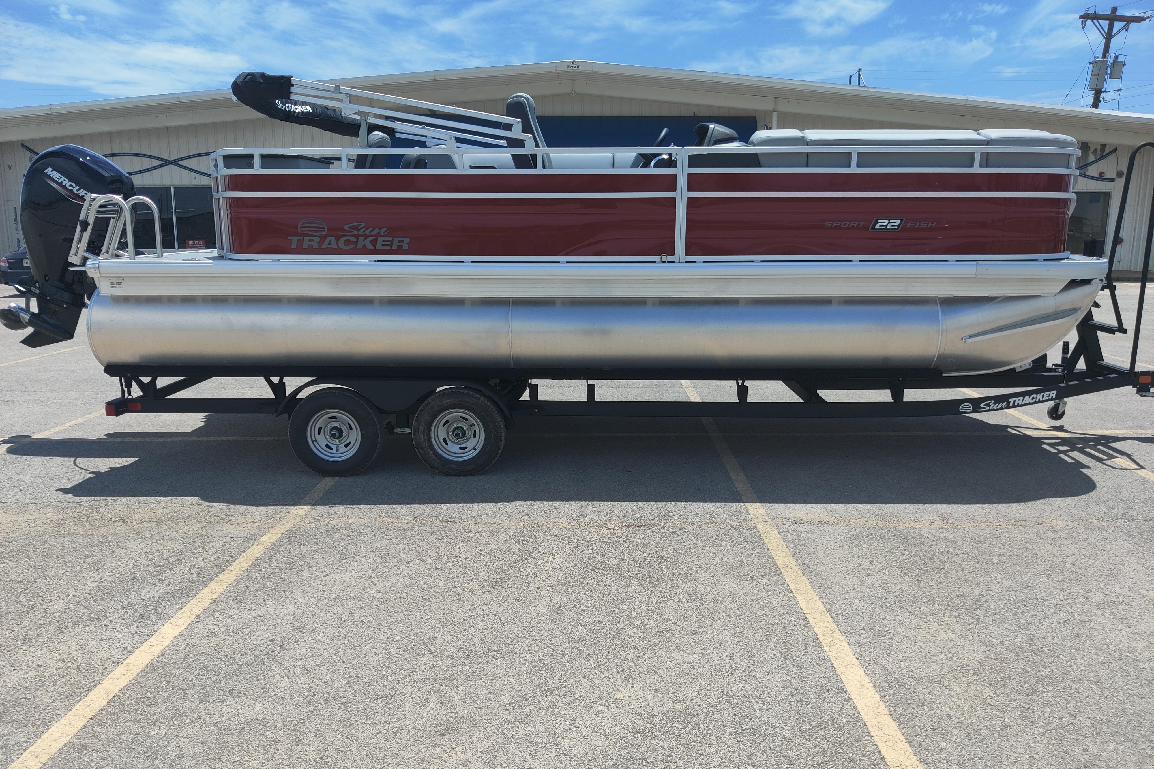 2026 Sun Tracker SportFish 22 DLX pontoon boat on trailer in parking lot.