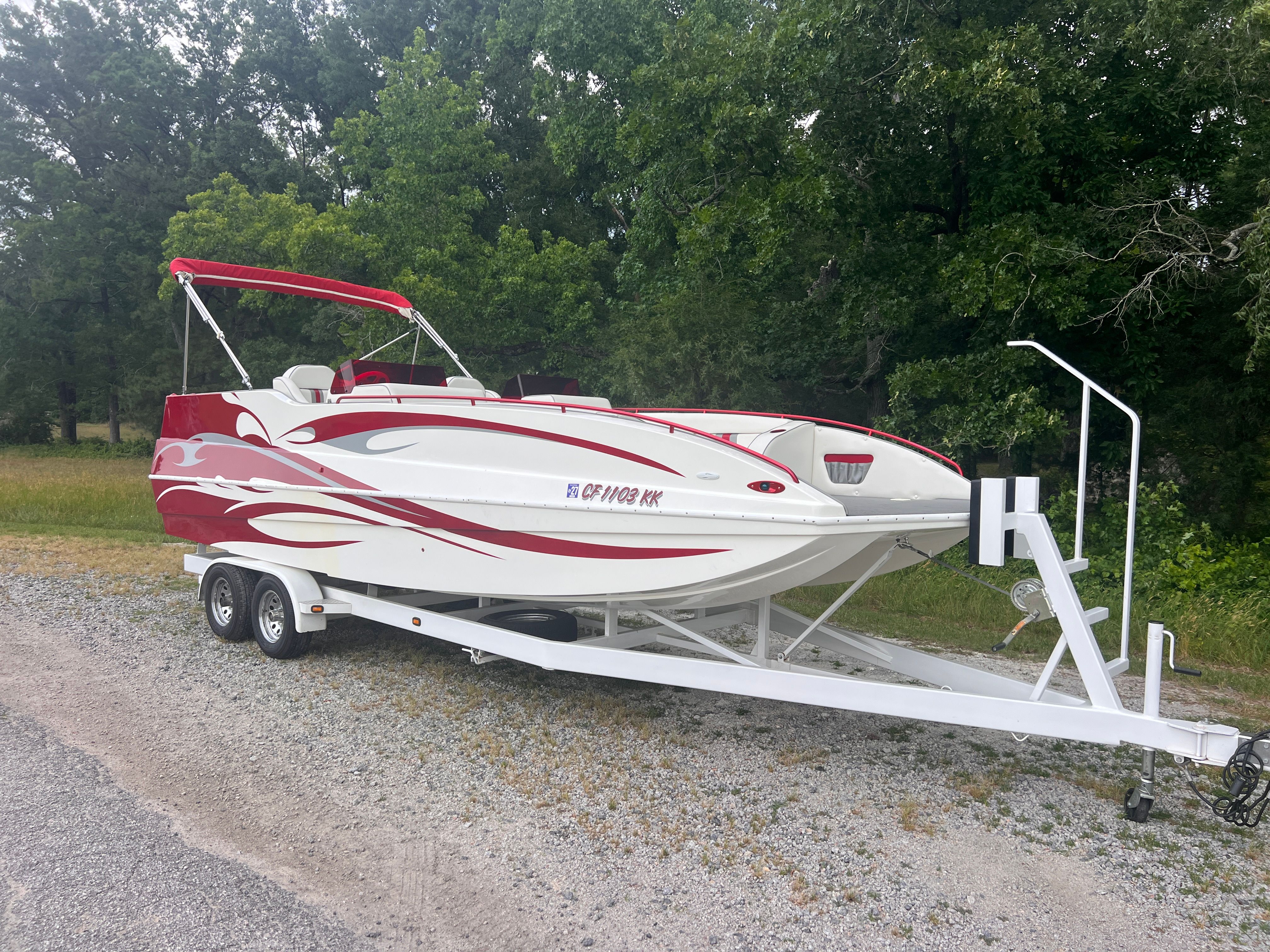 A white and red speedboat on a trailer, surrounded by trees.