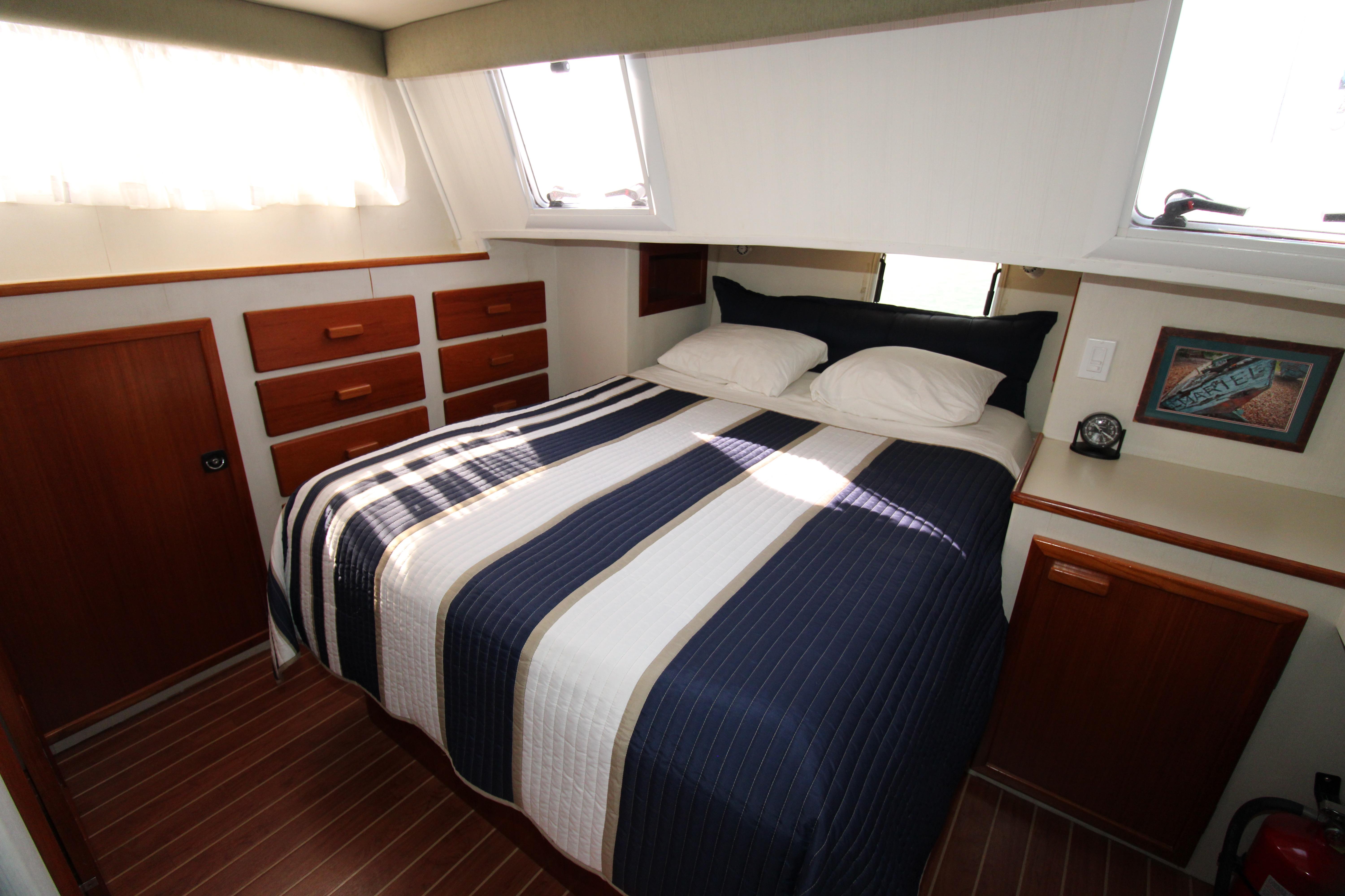 Cozy bedroom in 2000 Ricker 42 Classic yacht with striped bedding and wooden cabinetry.