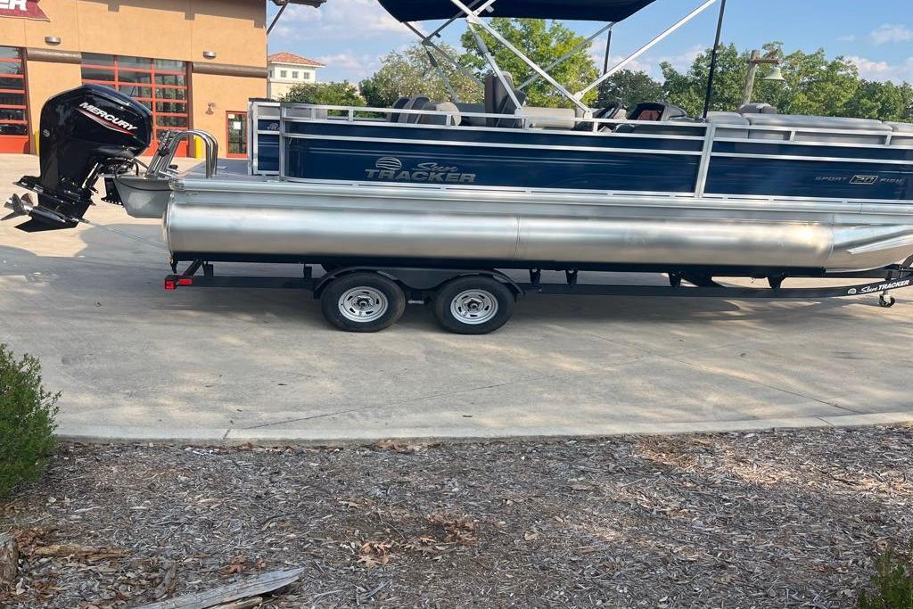 2026 Sun Tracker SportFish 20 DLX pontoon boat on trailer, parked outdoors.