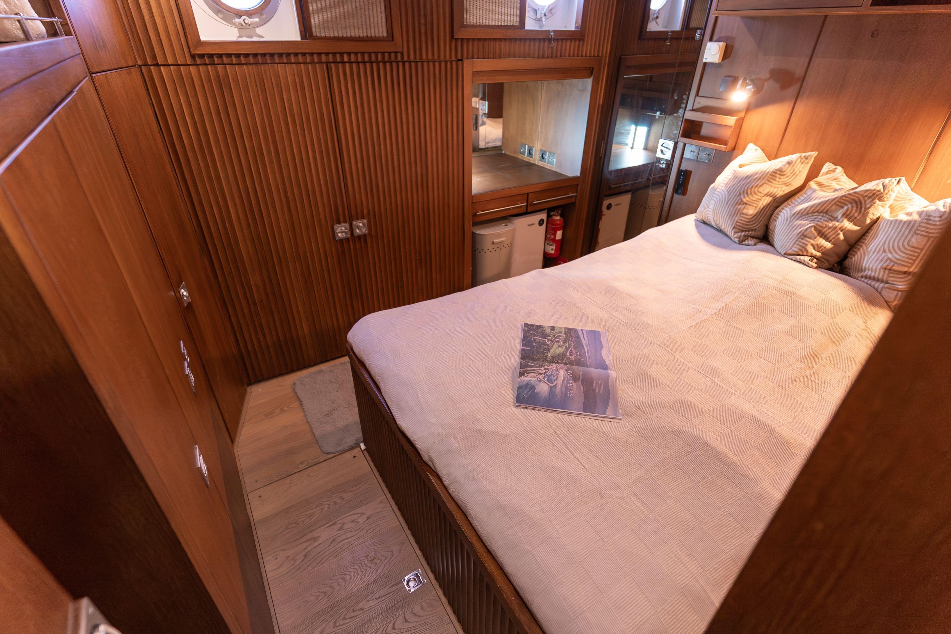Cozy wooden cabin interior with bed, pillows, and magazine on a 1967 Cammenga 61 yacht.