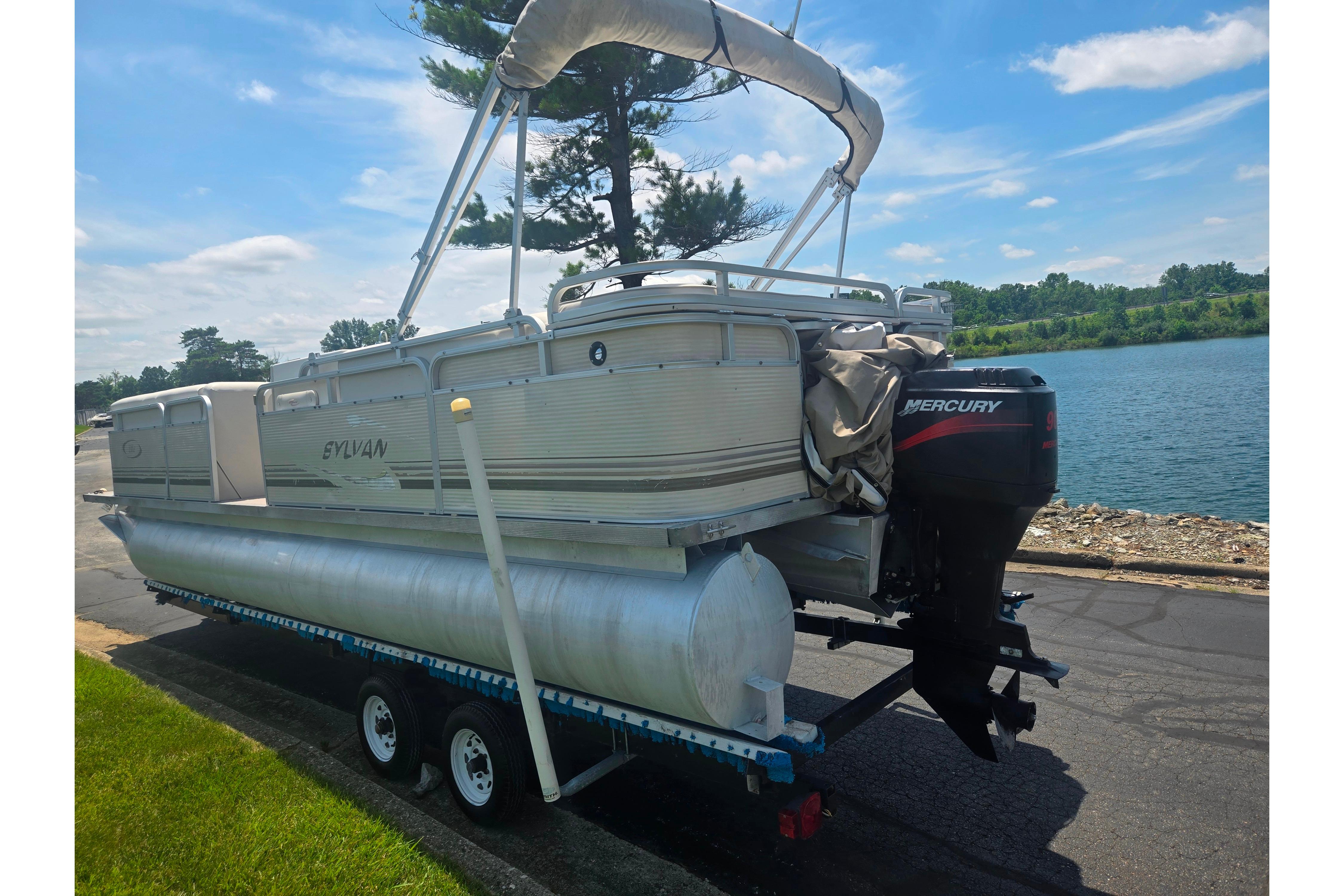 2000 Sylvan 824 Elite Cruise pontoon boat on trailer by a lake.